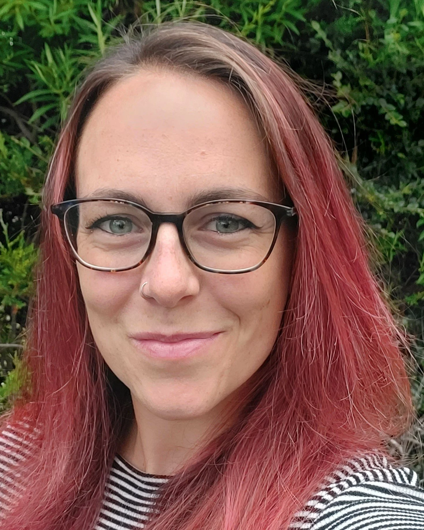 Cassie Hogg, counsellor with red hair and glasses, smiles while outside