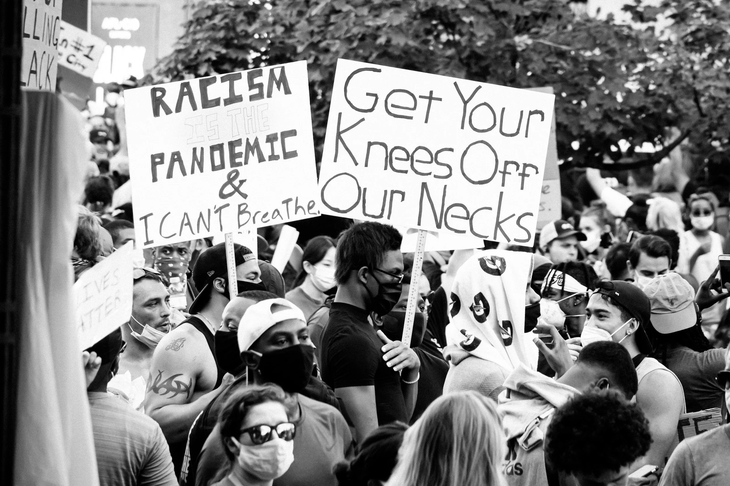 Protestors hold signs saying 'Racism is the Pandemic', 'I can't breathe' and 'Get your knees off our necks' in response to Floyd's murder in 2020.