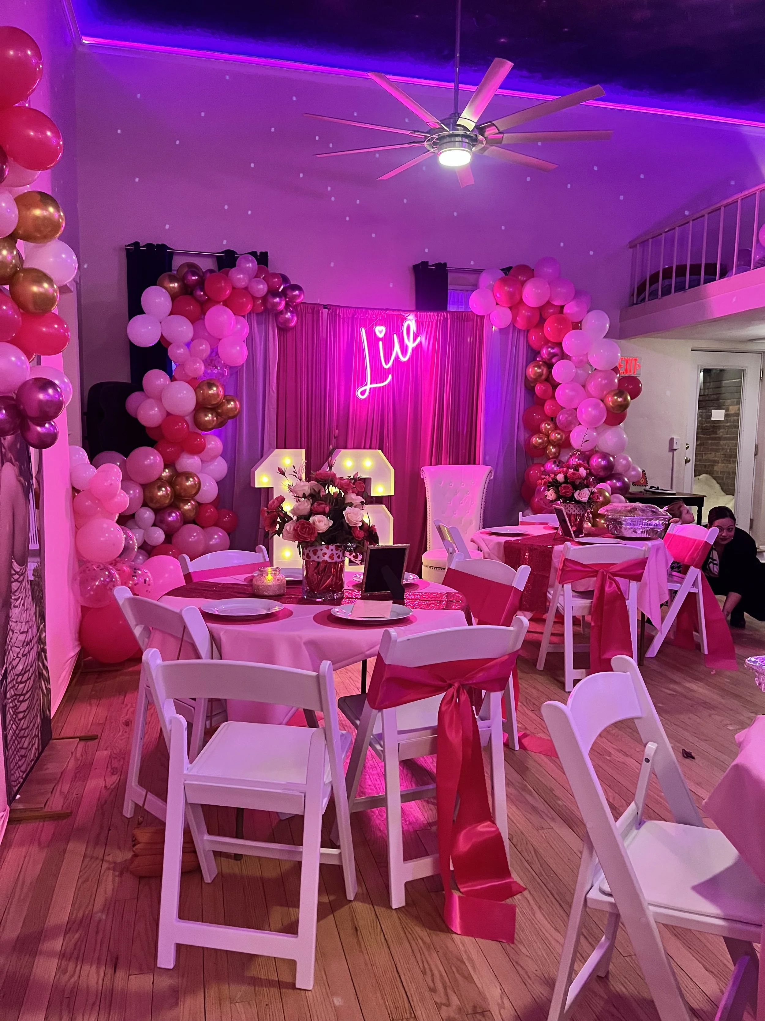 Room with purple and pink lighting, moon and star decorations hanging from the ceiling, small round tables on wooden floor.