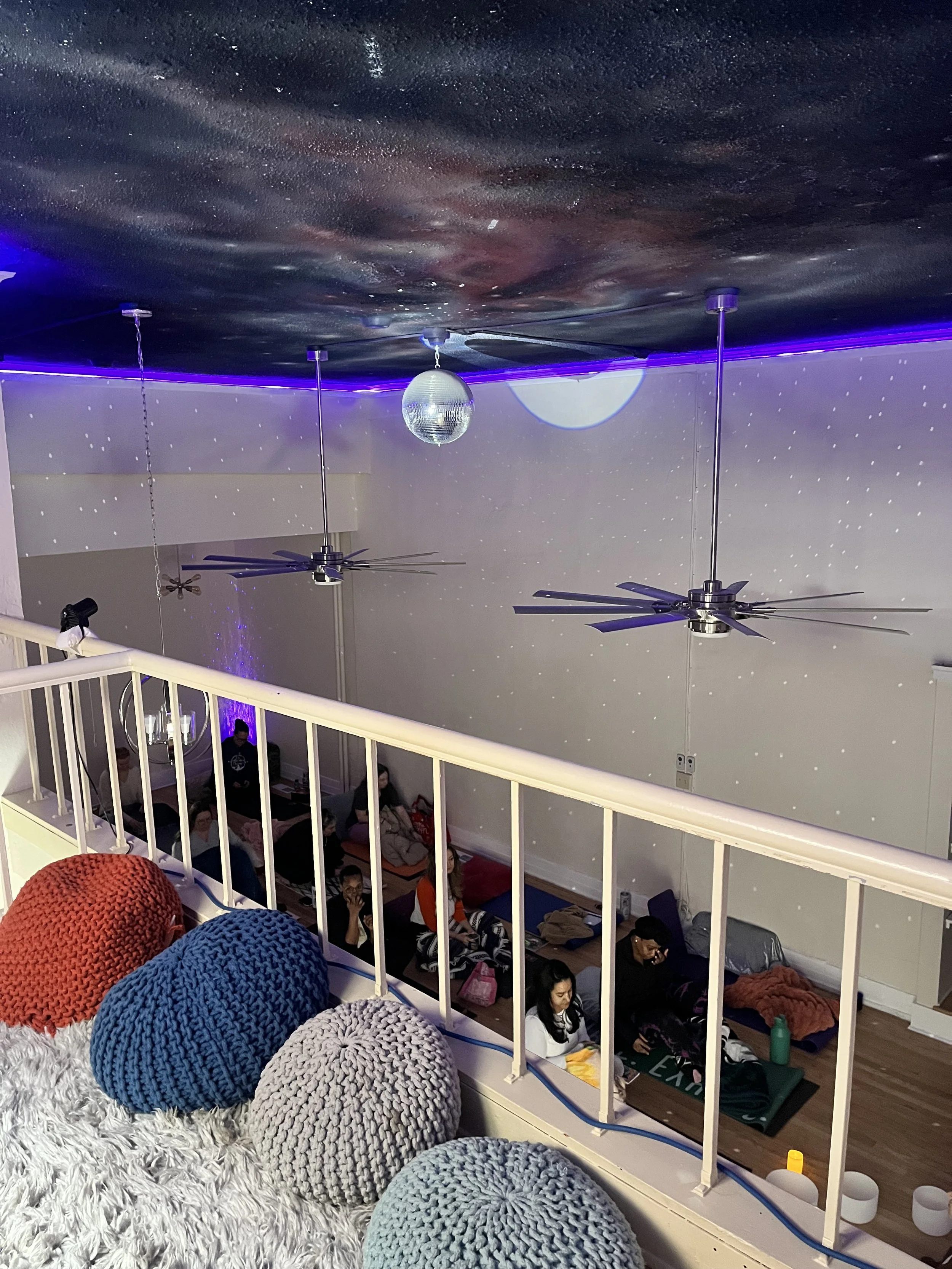 Indoor party or dance room with disco ball and starry light projections on the ceiling and walls, with a wooden floor.