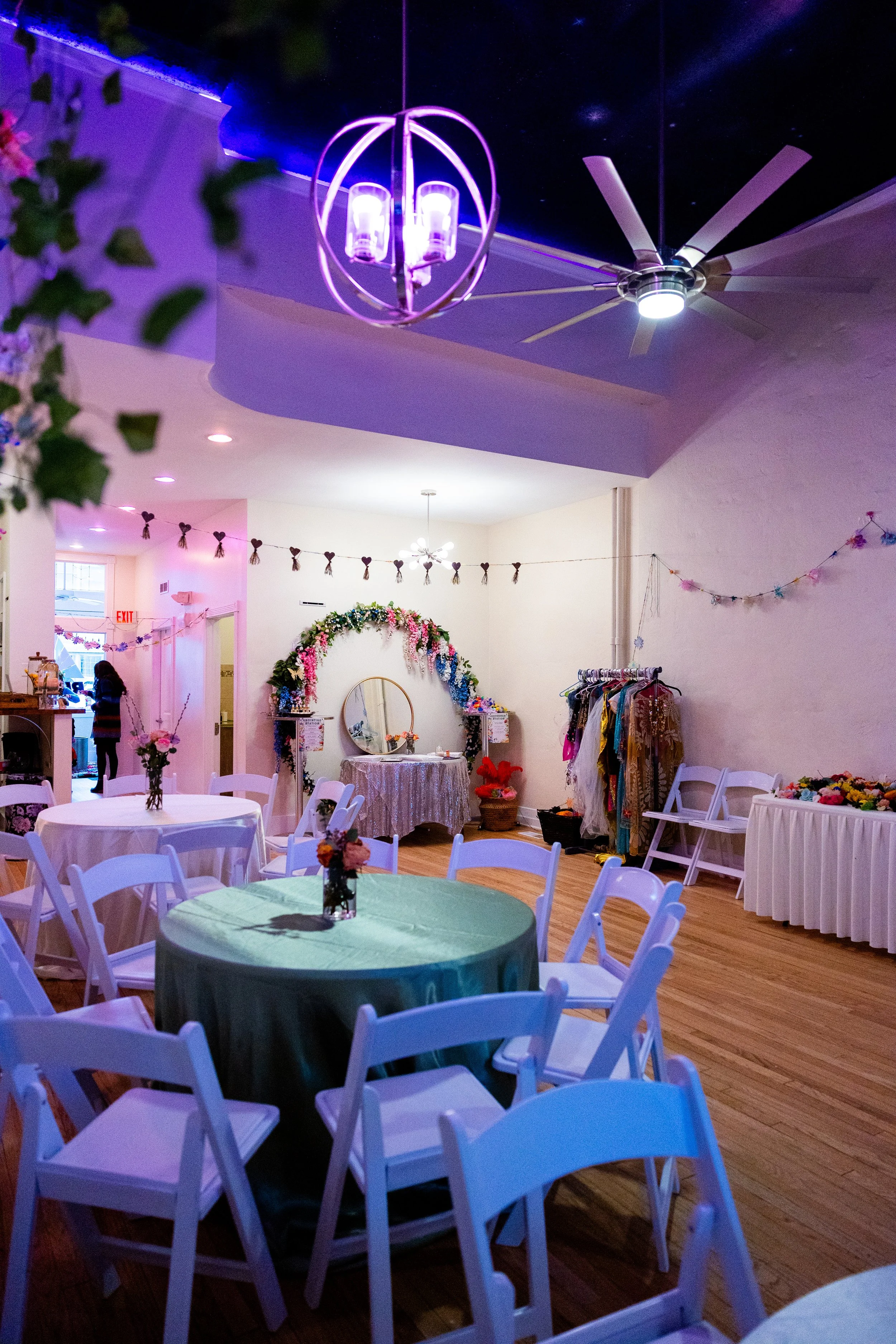 A banquet hall decorated for an event with tables covered with tablecloths, chairs, and flowers
