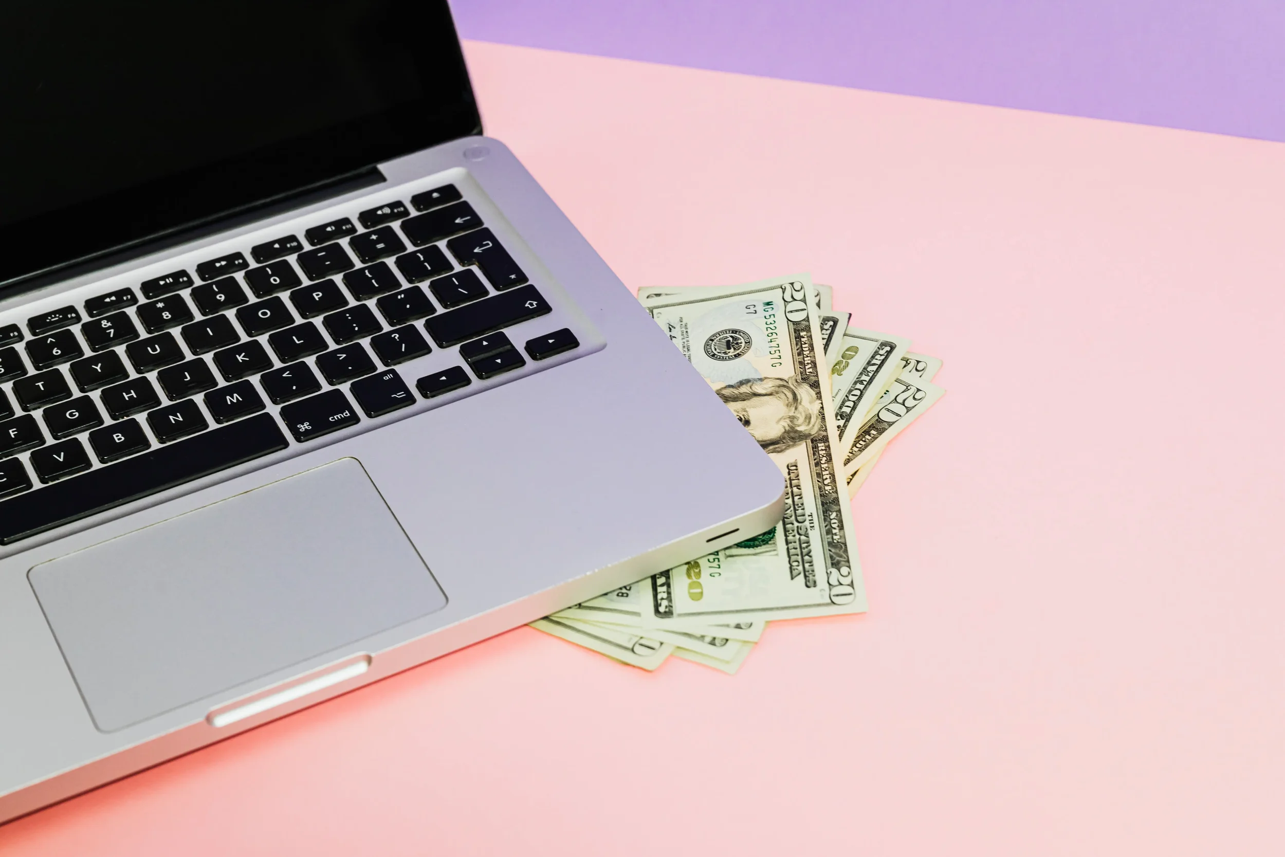Cash tucked beneath a computer represents scalable passive income ideas for therapists, including courses, digital resources, memberships, and other non-session-based offers.