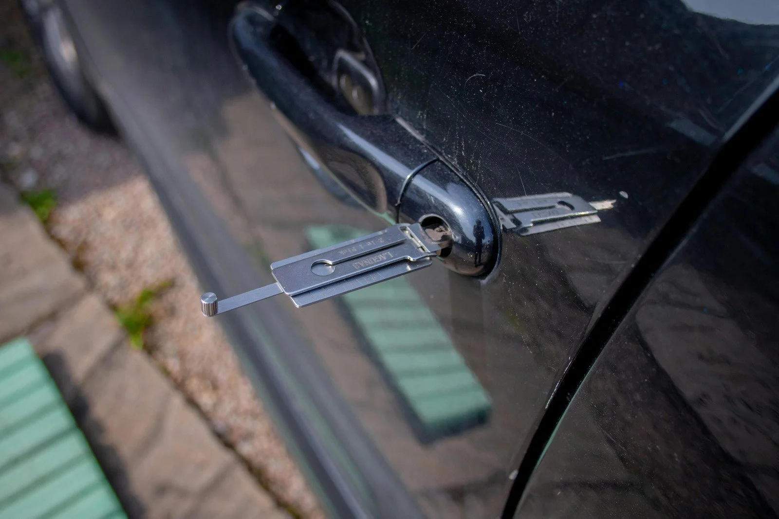A lockPicking set inserting a tool into a car door lock on a black vehicle.