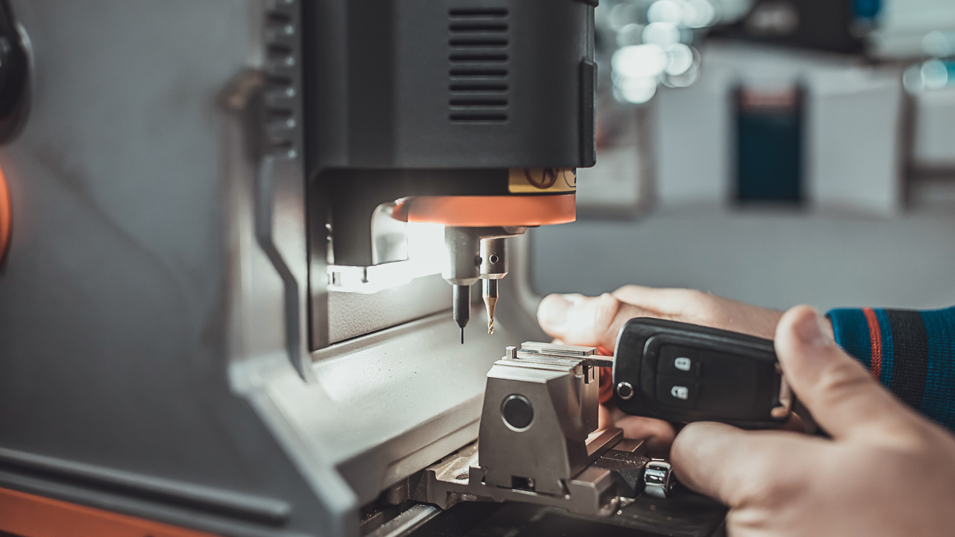 A person holding a car key fob near a machine that appears to be involved in manufacturing or machining a metal part.