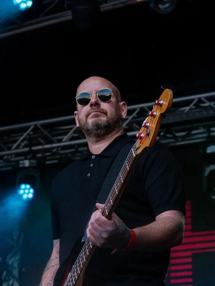 A man with sunglasses playing a bass guitar on stage at a music concert.