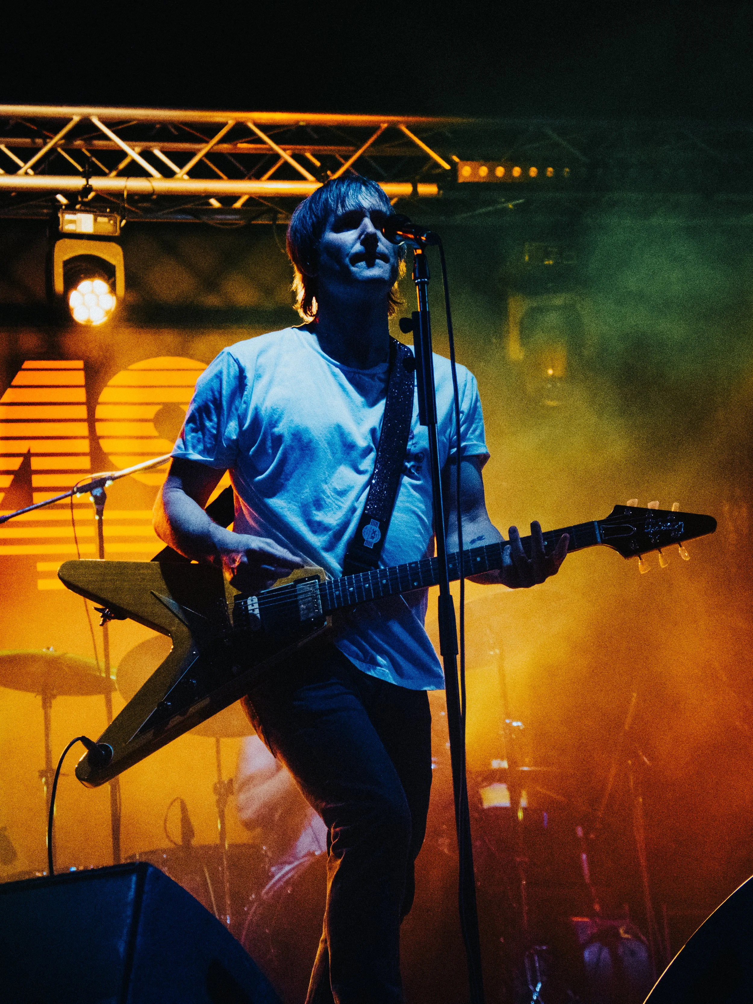 Tim Wheeler lead singer & guitarist from Ash performing on stage at festival too Kings Lynn with a guitar, illuminated by vibrant stage lights with a smoky atmosphere.