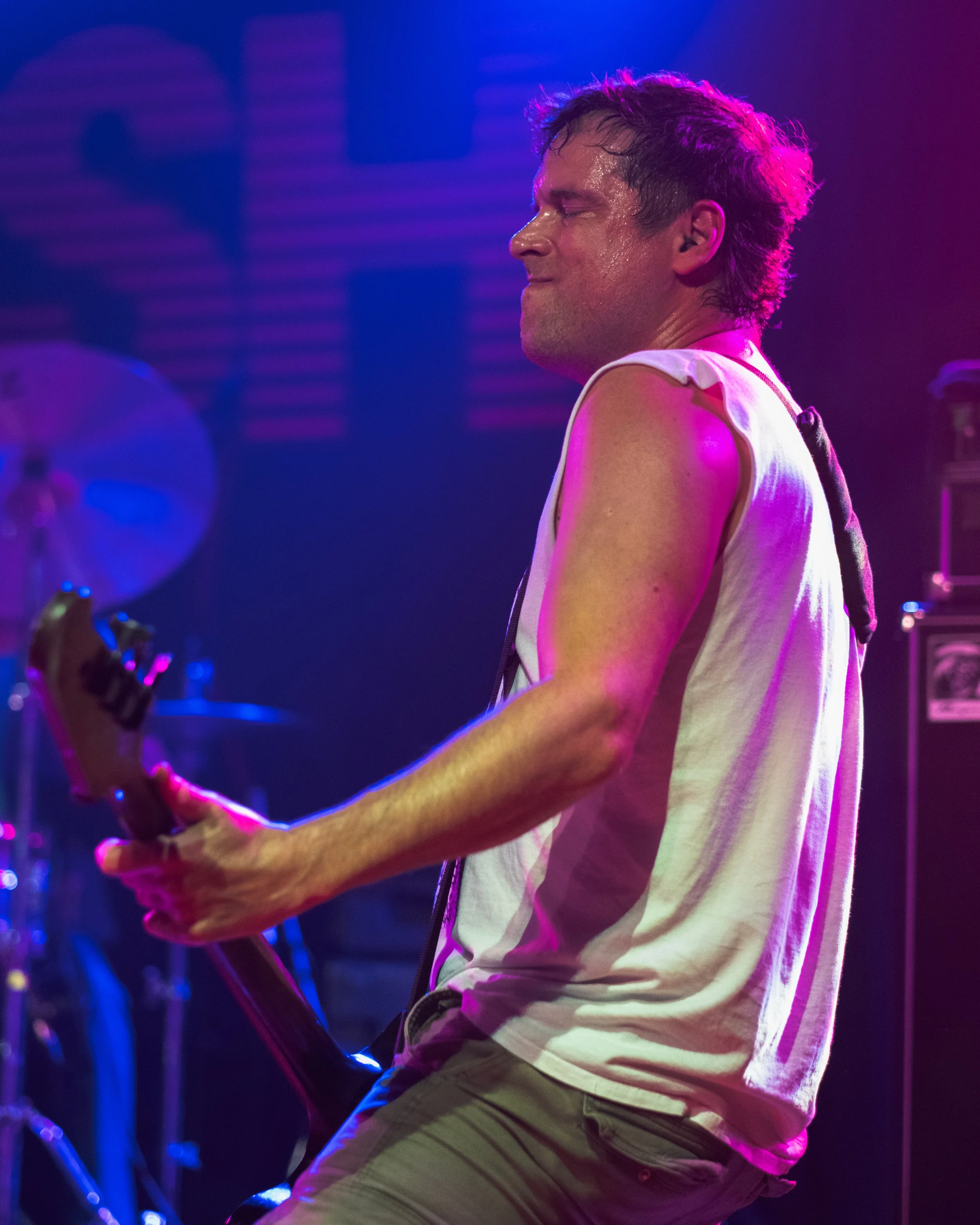 A man playing an electric guitar on stage, sweating and enjoying the performance, with colorful stage lighting.