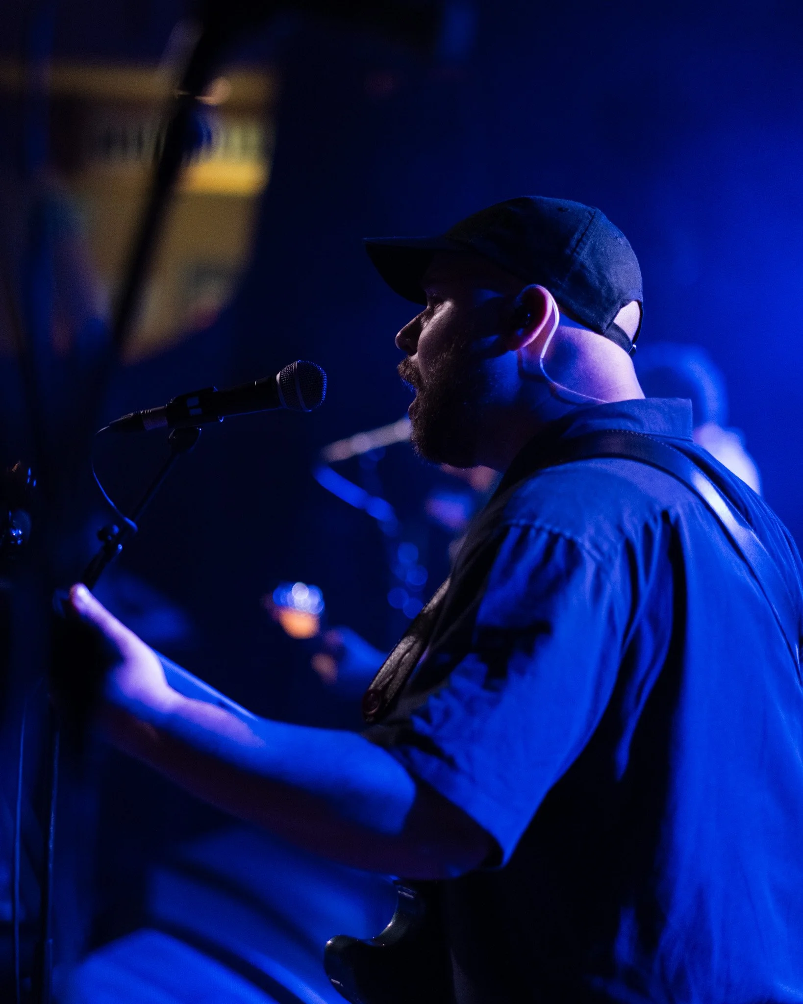 Man playing guitar and singing into a microphone on stage with blue lighting