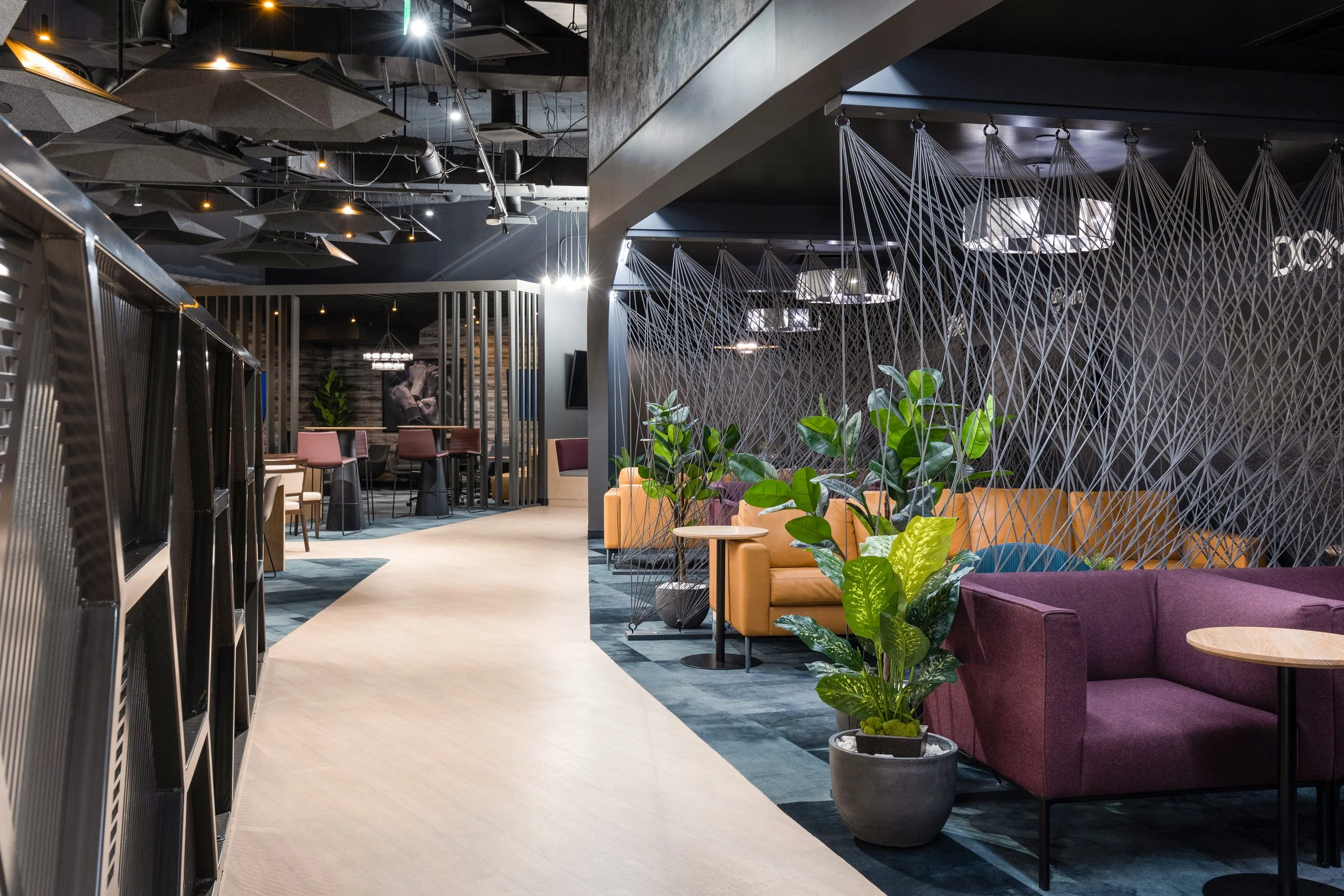 Modern lounge area with colorful sofas, green plants, and decorative string art dividers inside a contemporary building.