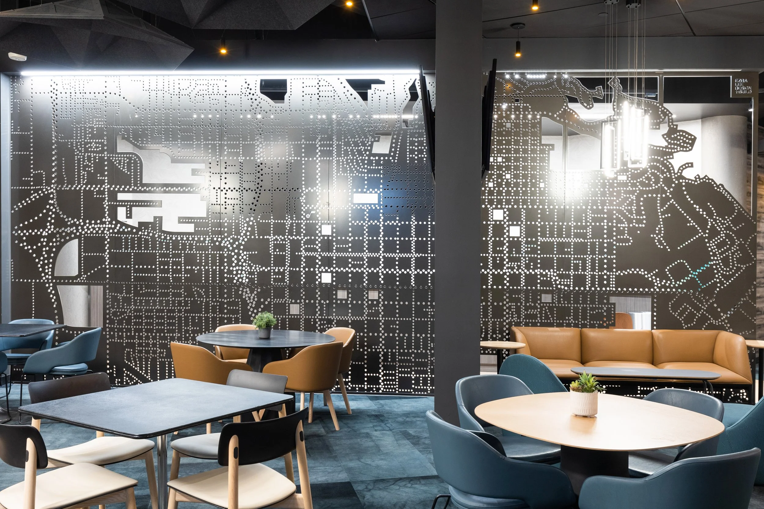 Modern cafe or lounge with a decorative perforated metal wall featuring a map and a horse design, surrounded by round tables and chairs, some with potted plants for decor.
