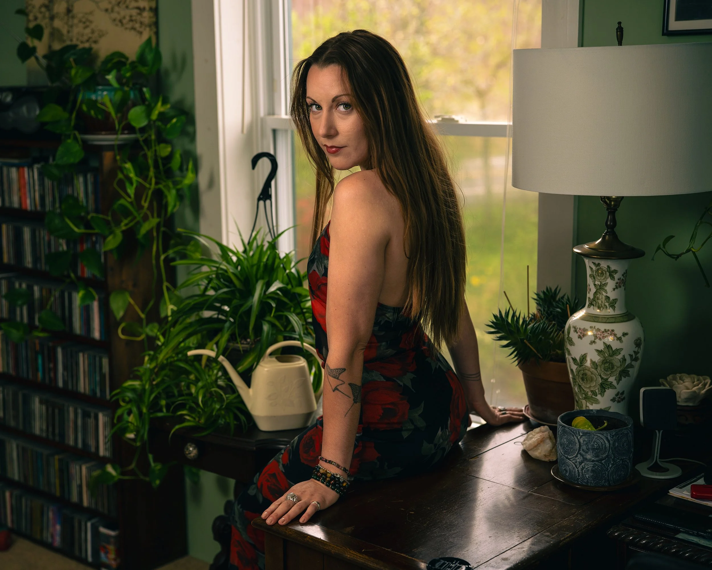 Louka wearing a red dress sitting on a wooden table in a room with plants and green wallpaper.