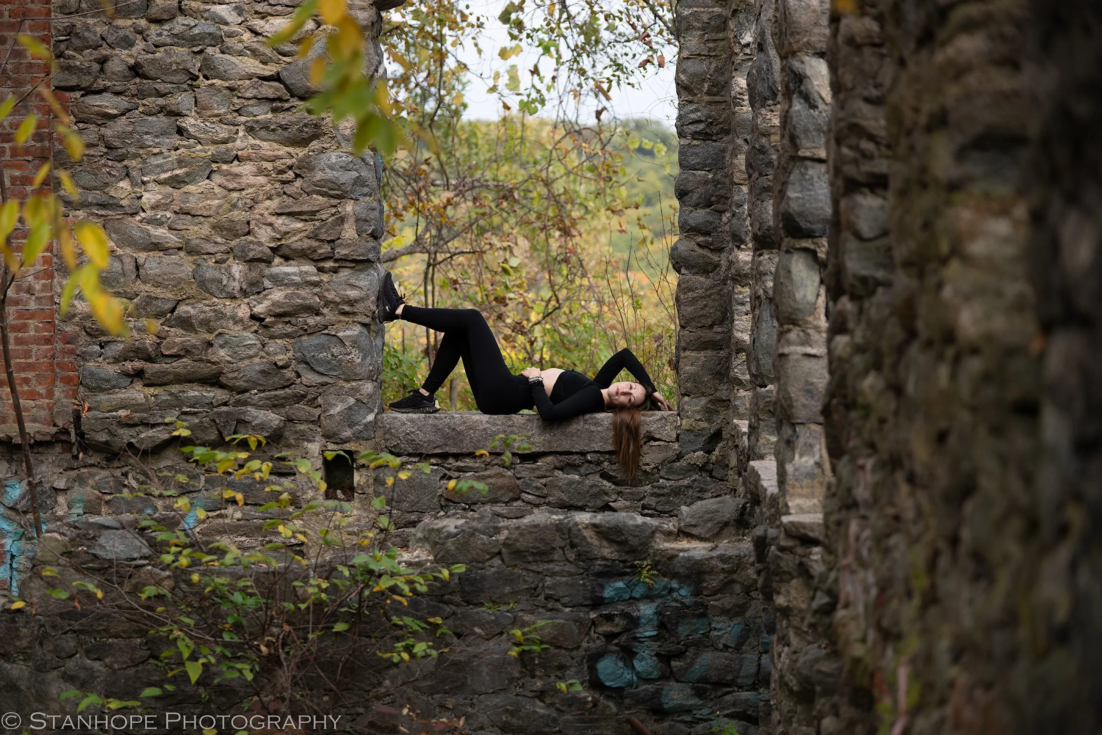Louka wearing all black laying on her back in a cobblestone structure.