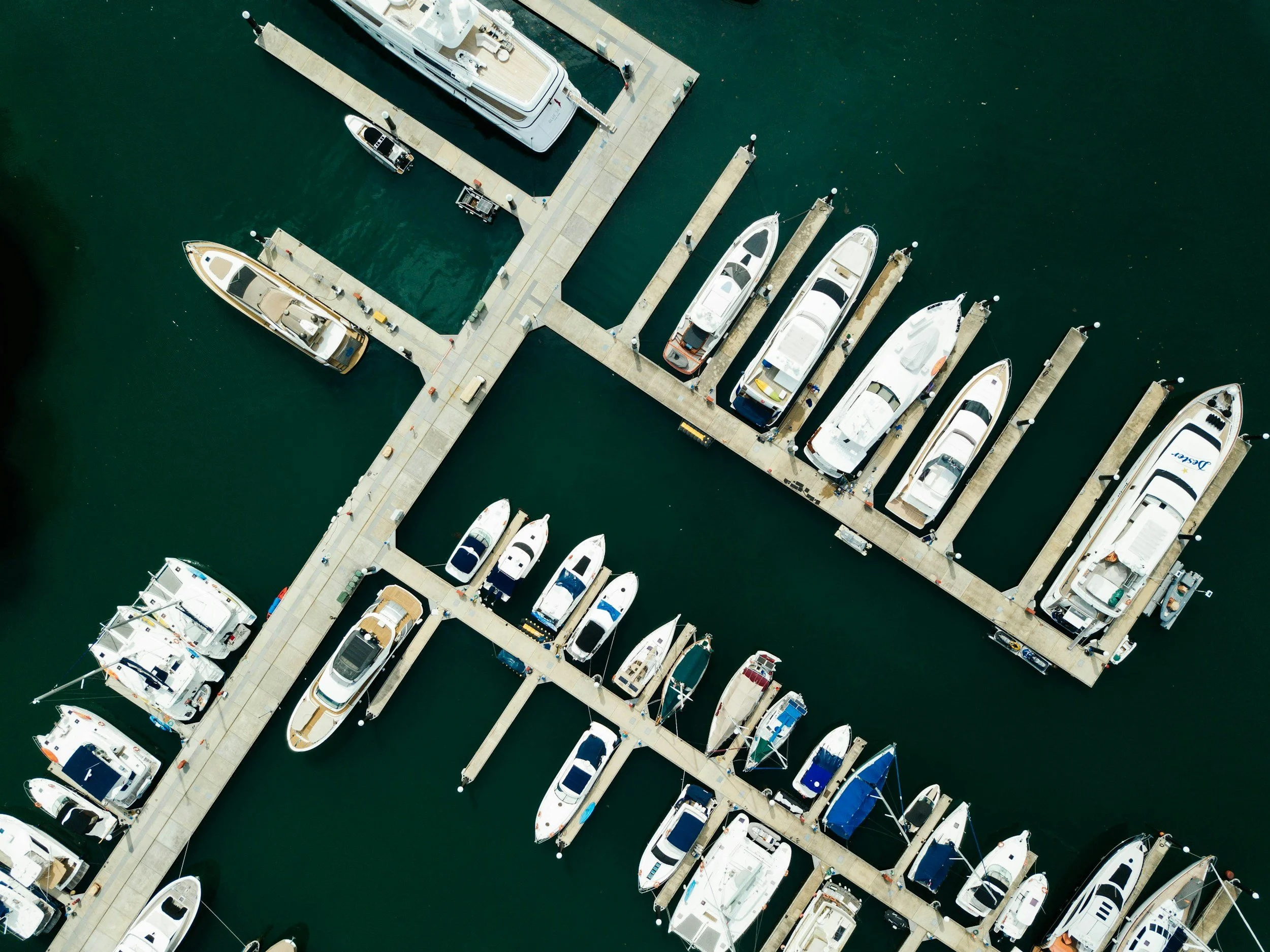 Aerial view of a marina with multiple boats docked along the piers in green water.