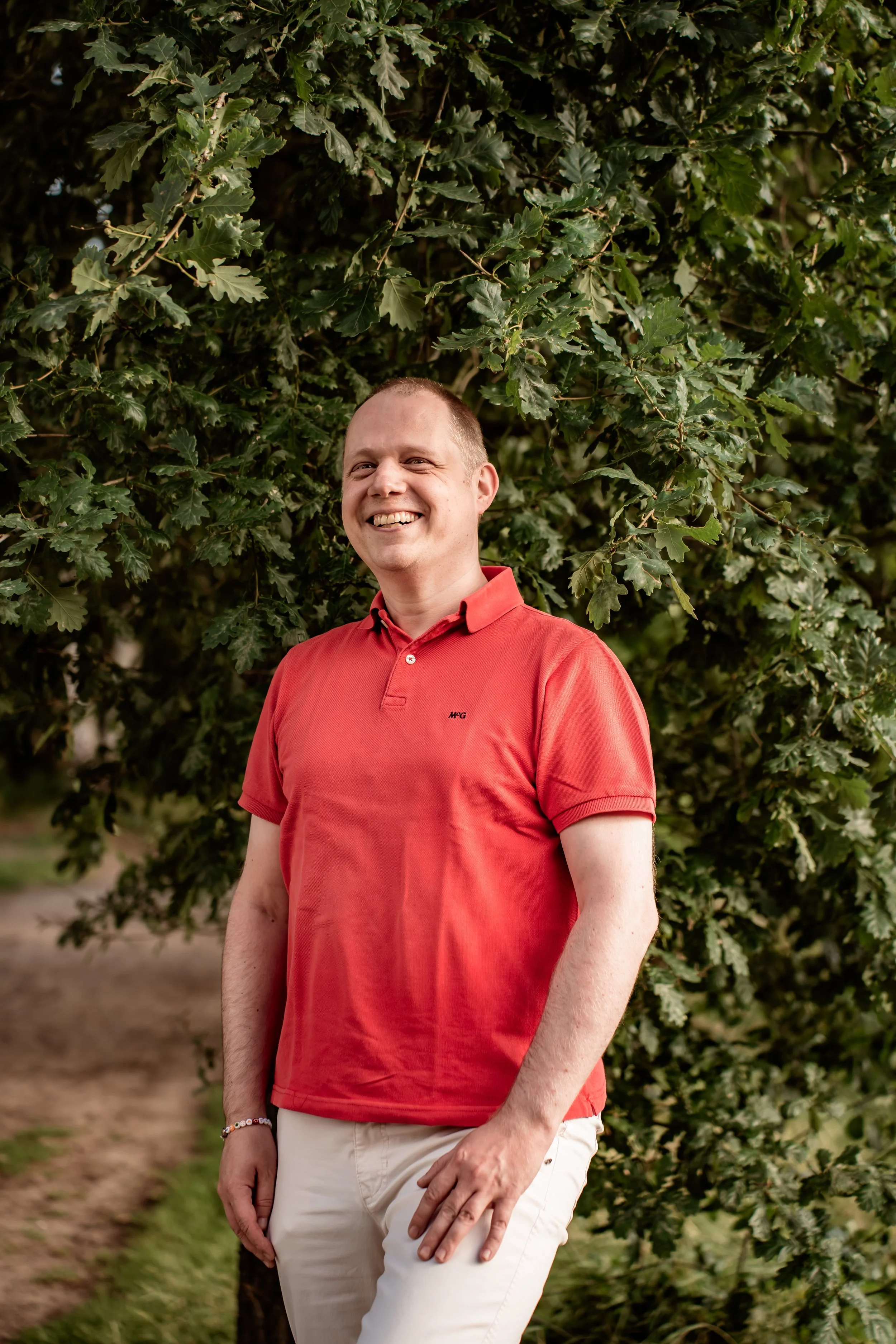Een glimlachende Maarten Wauters (de Nuchtere Mysticus) in een rode poloshirt, staand in een groene, bosrijke natuurlijke omgeving.