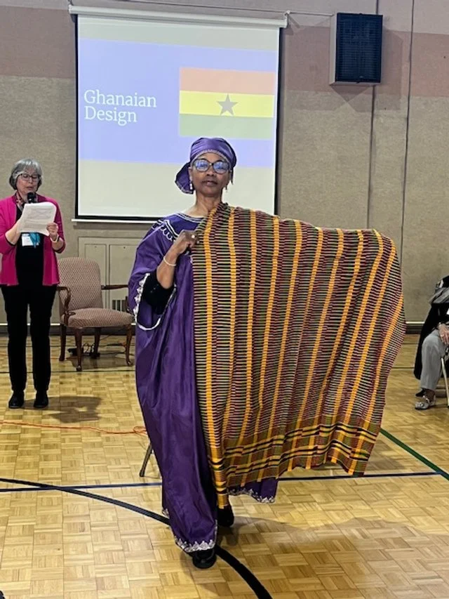 A woman in traditional Ghanaian attire holding a Kente cloth in a conference or presentation setting.