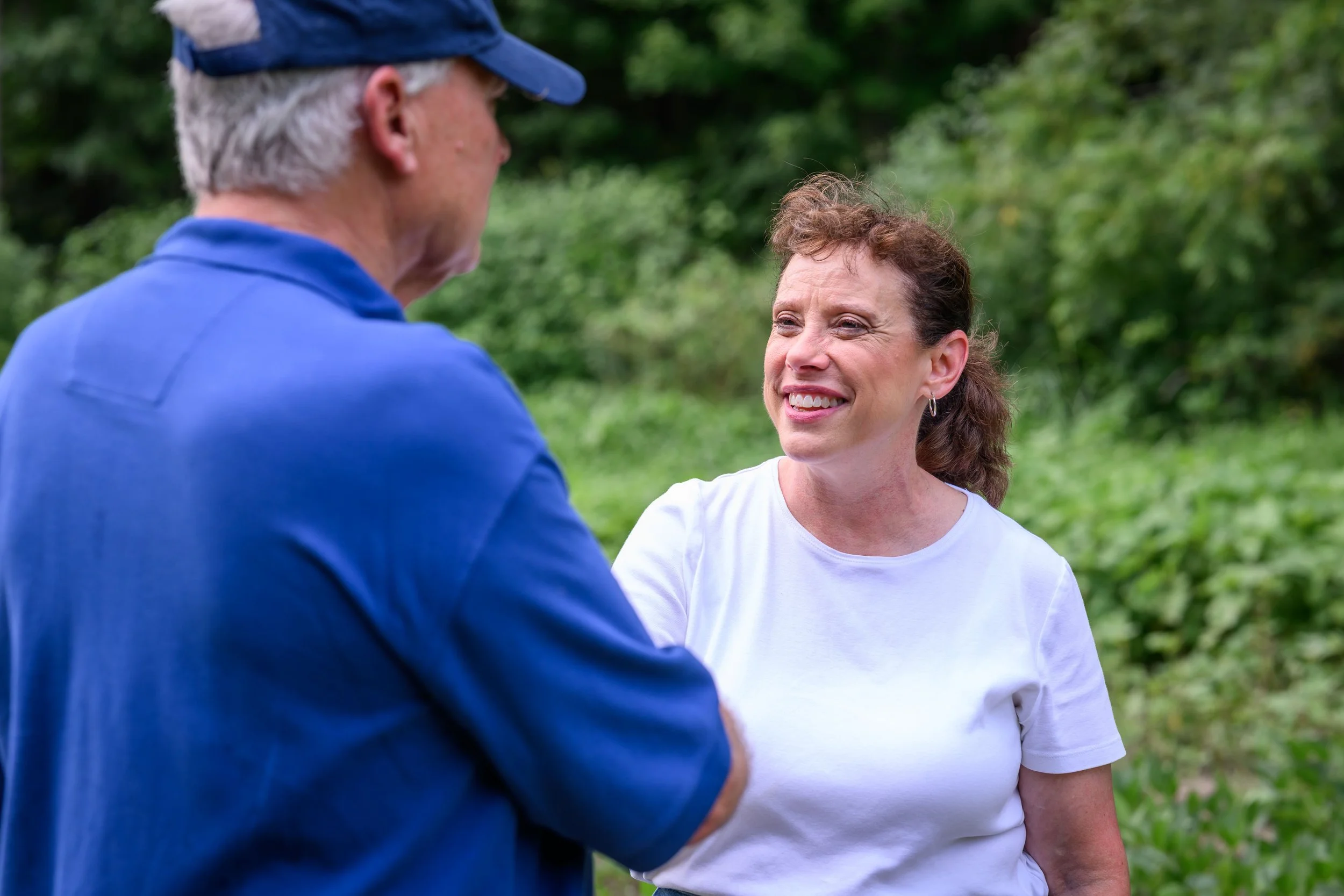 Amy Huffman Oliver shakes hands with a farmer in front a field.