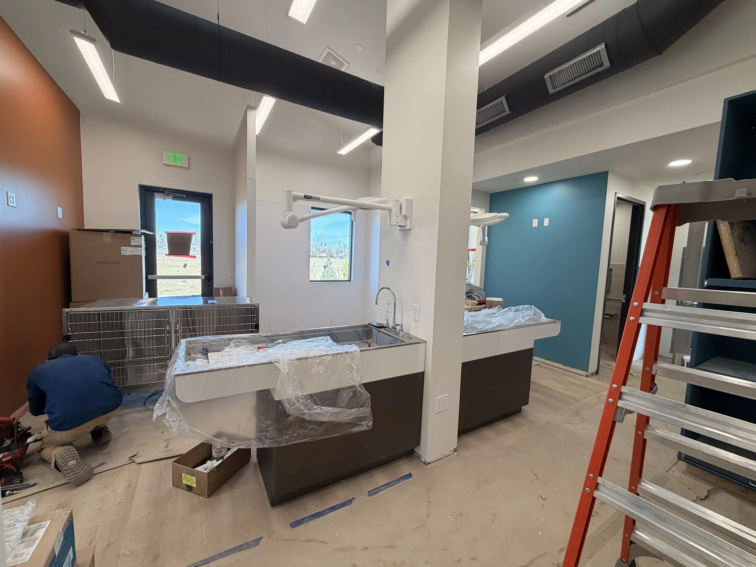 Construction worker installing fixtures in a commercial kitchen or bar area with new sinks, cabinetry, and unfinished flooring.