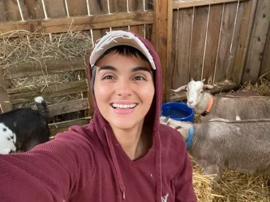 Niquelle taking a selfie with goats in a barn or stable.