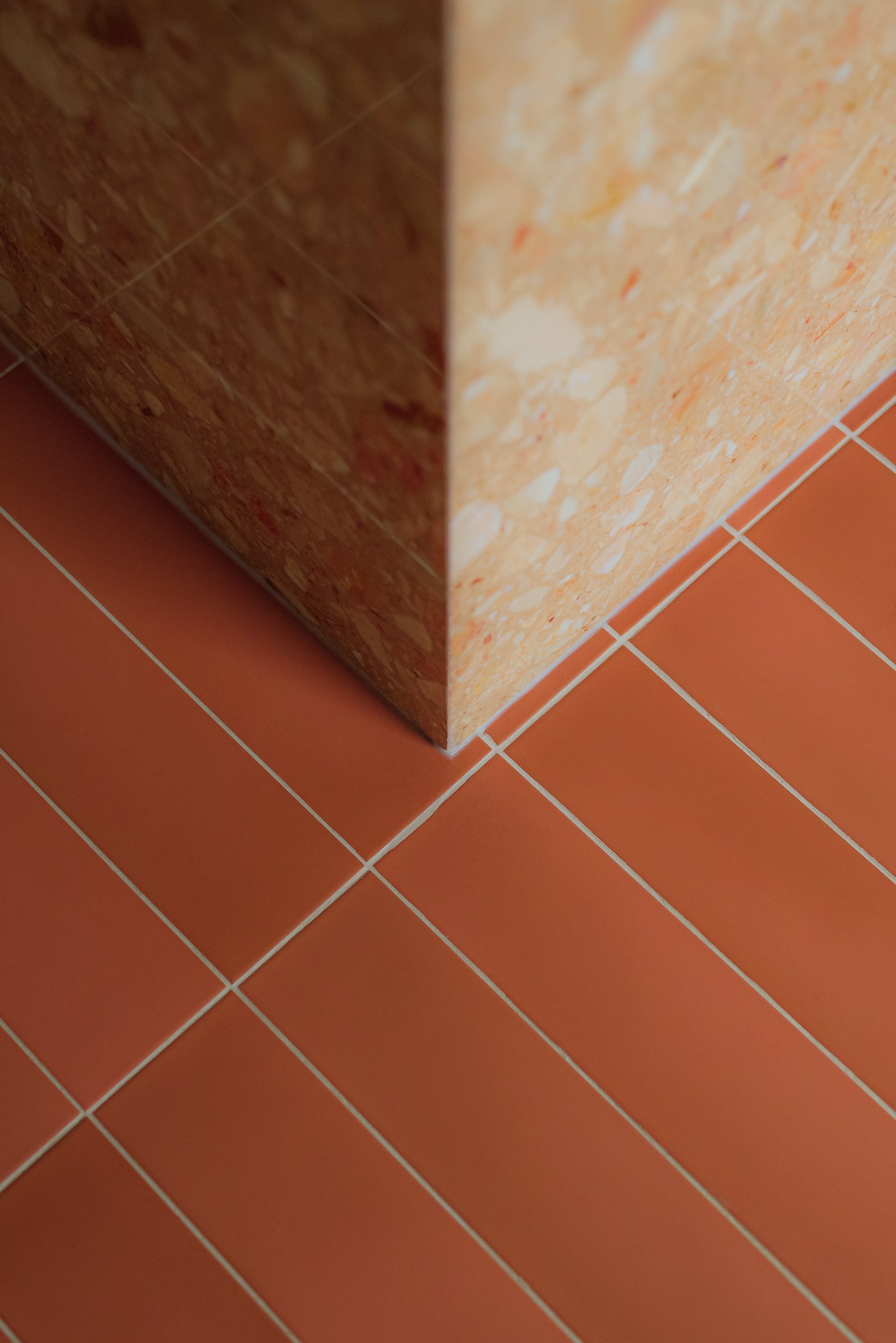 Close-up of a corner between orange ceramic floor tiles and a brick wall with a rough texture.