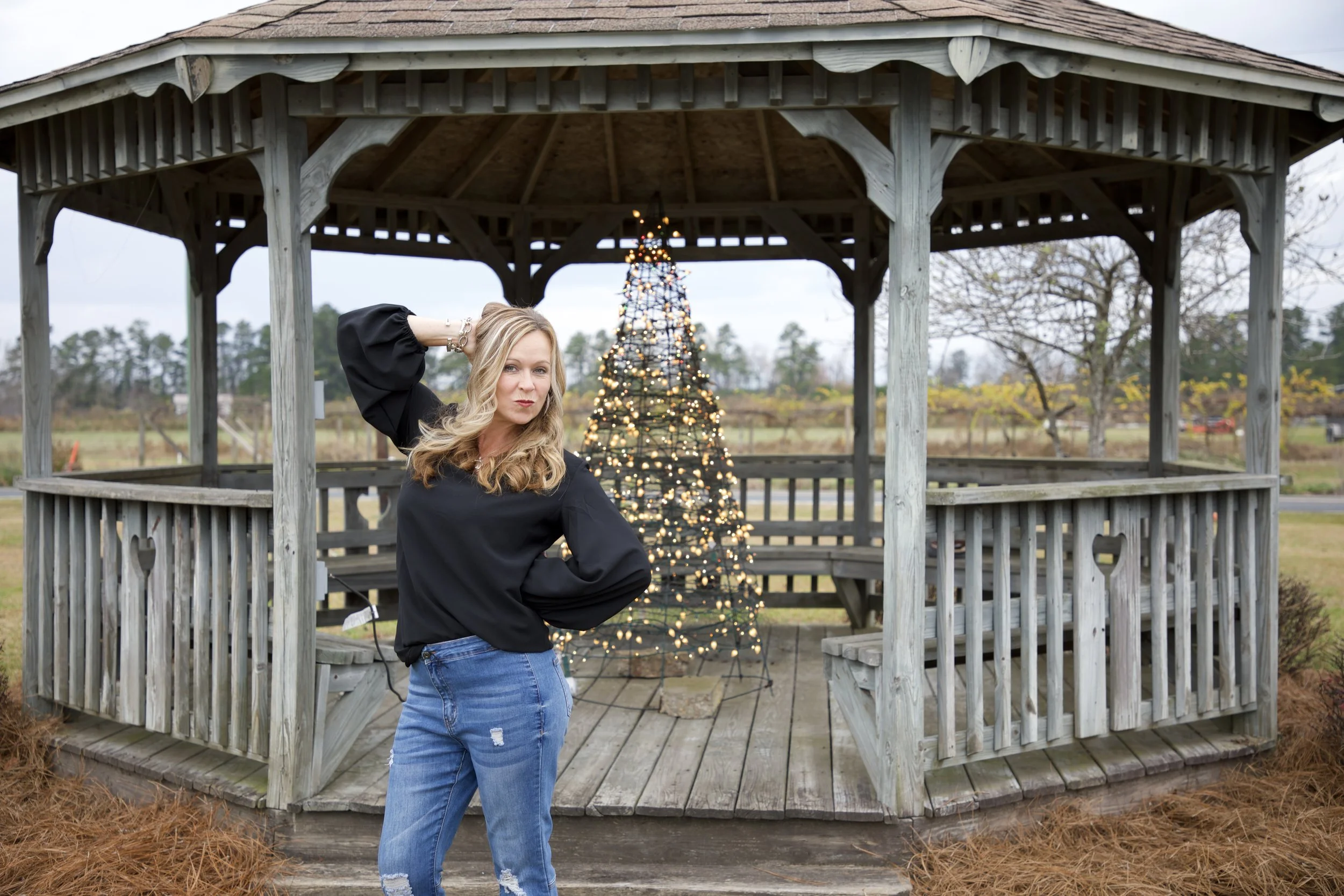 A woman standing in front of a decorated outdoor gazebo with a Christmas tree in the background.