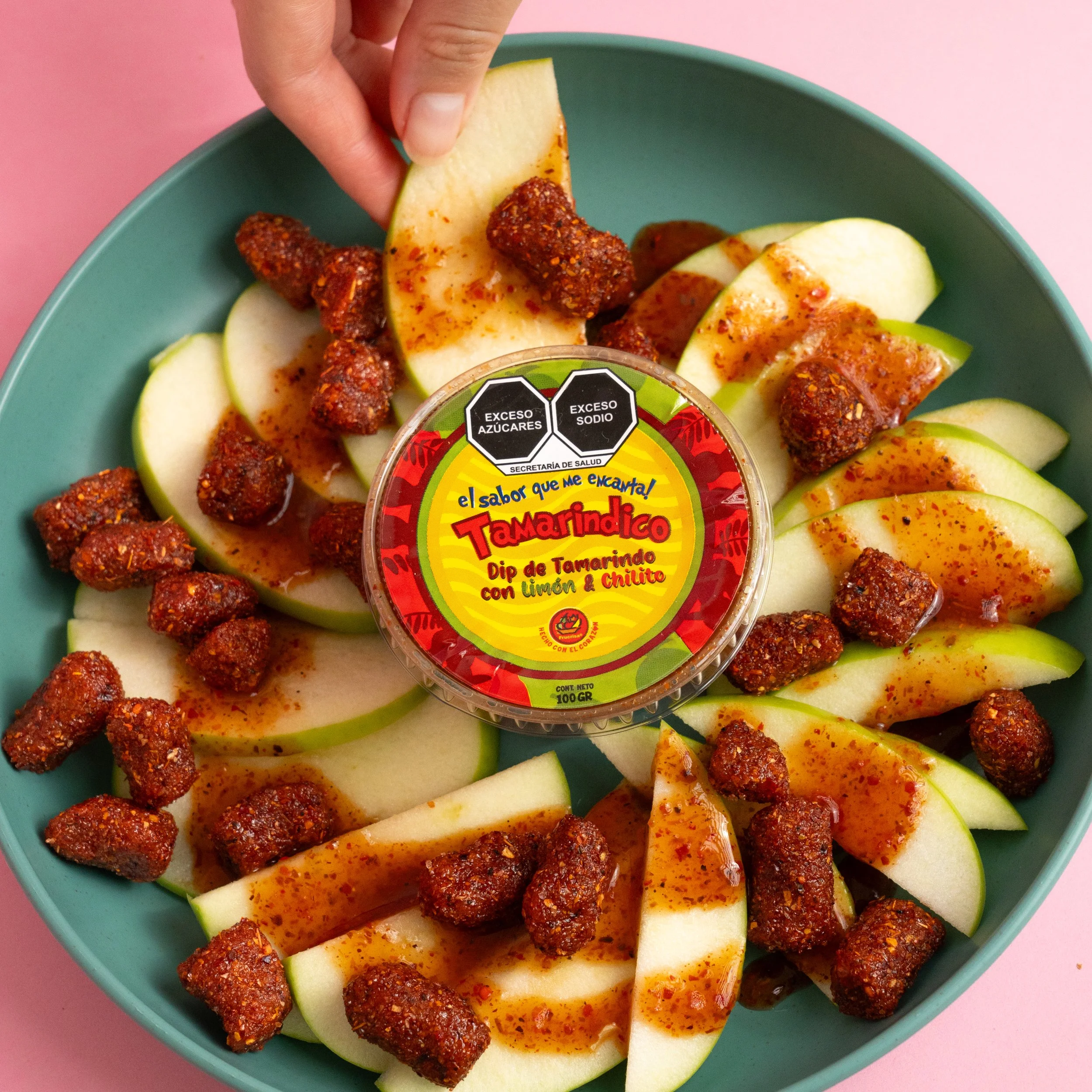 Un plato con rebanadas de manzana, bolitas ricas de frutas y chamoy y chilito con salsa dip chamoy de Tamarindo con limón y chile, además un envase de dip de Tamarindo en el centro.
