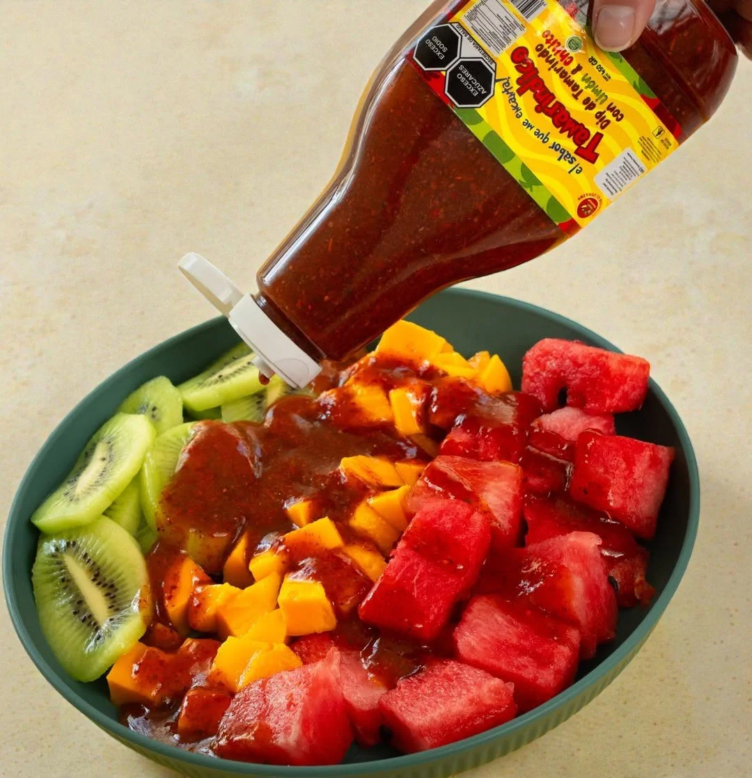 Fruta en un tazón con kiwi, mango y sandía, y salsa dip de chamoy vertida desde una botella liquida de salsa.