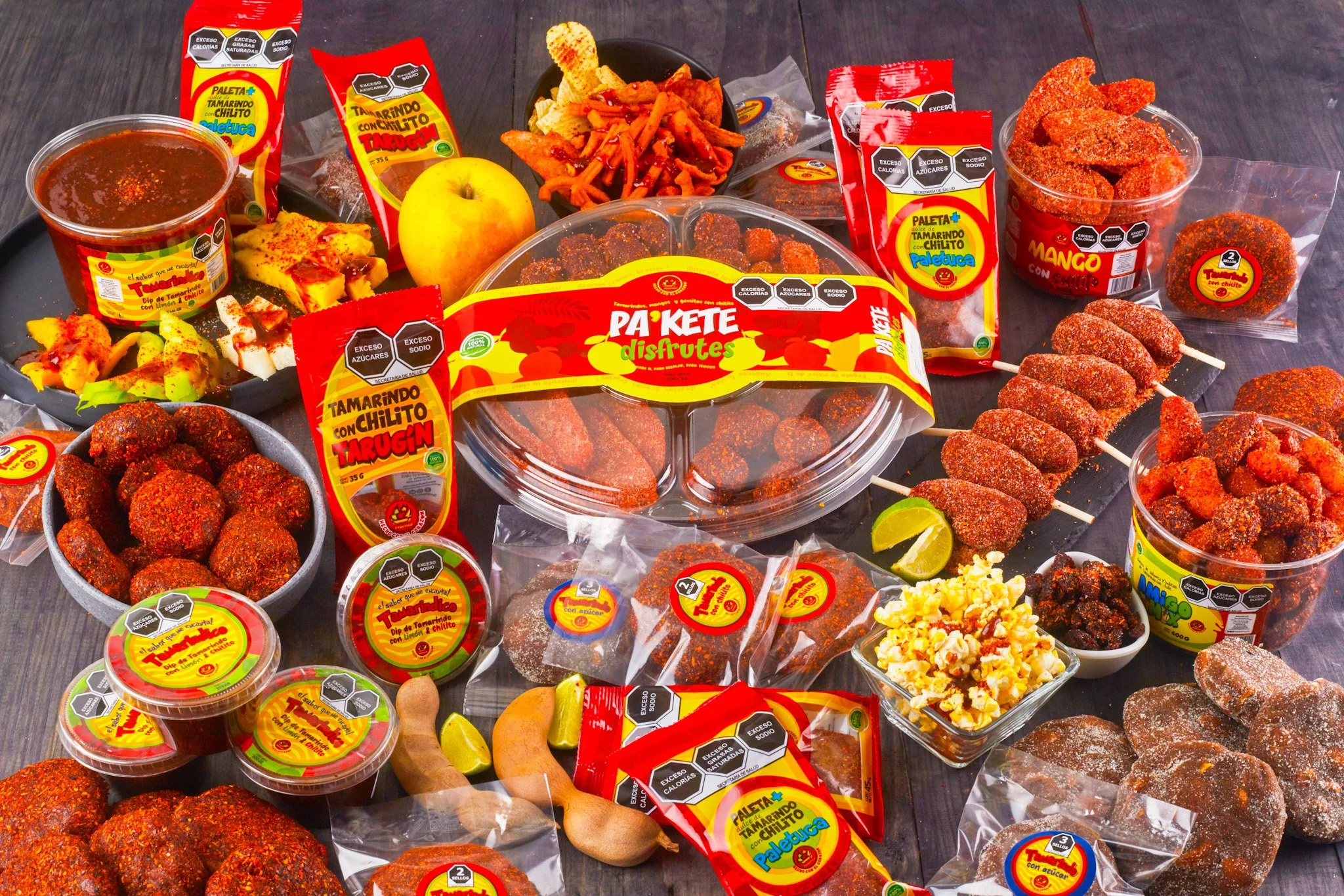 Variedad de productos de dulces mexicanos, artesanales y típicos, incluyendo tamarindo con chile, dulces y snacks en envases de colores rojo, amarillo y transparentes, con etiquetas y empaques decorados. Fruta natural enchilada con sabor dulce picoso