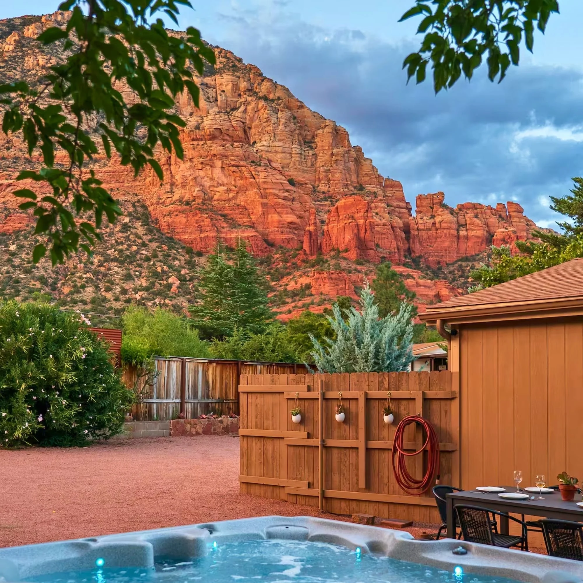 A backyard with a hot tub, table set for outdoor dining, and a mountain landscape with red rock formations.