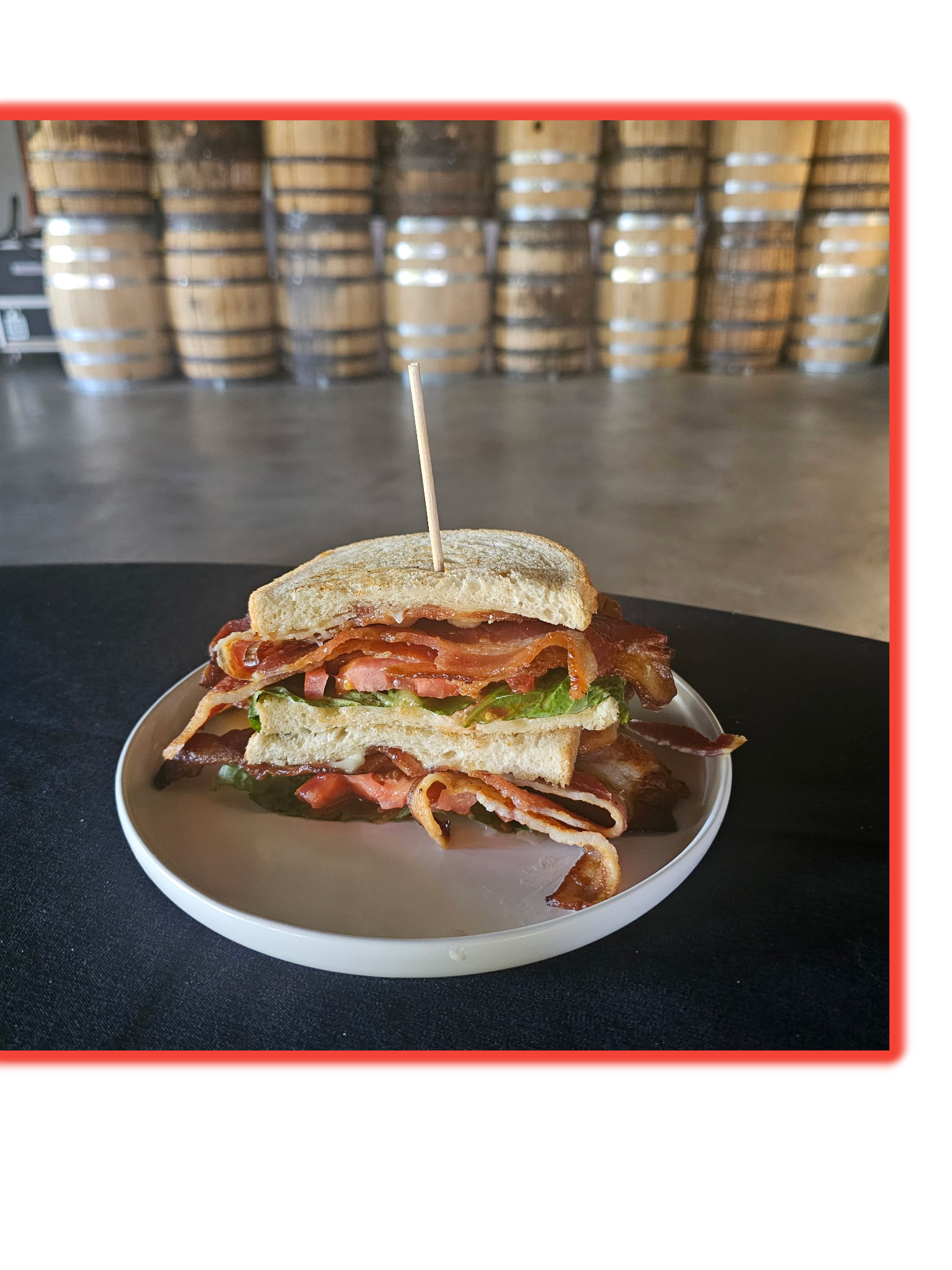 Bacon, lettuce, tomato, and sandwich bread on a white plate, with a background of stacked barrels.