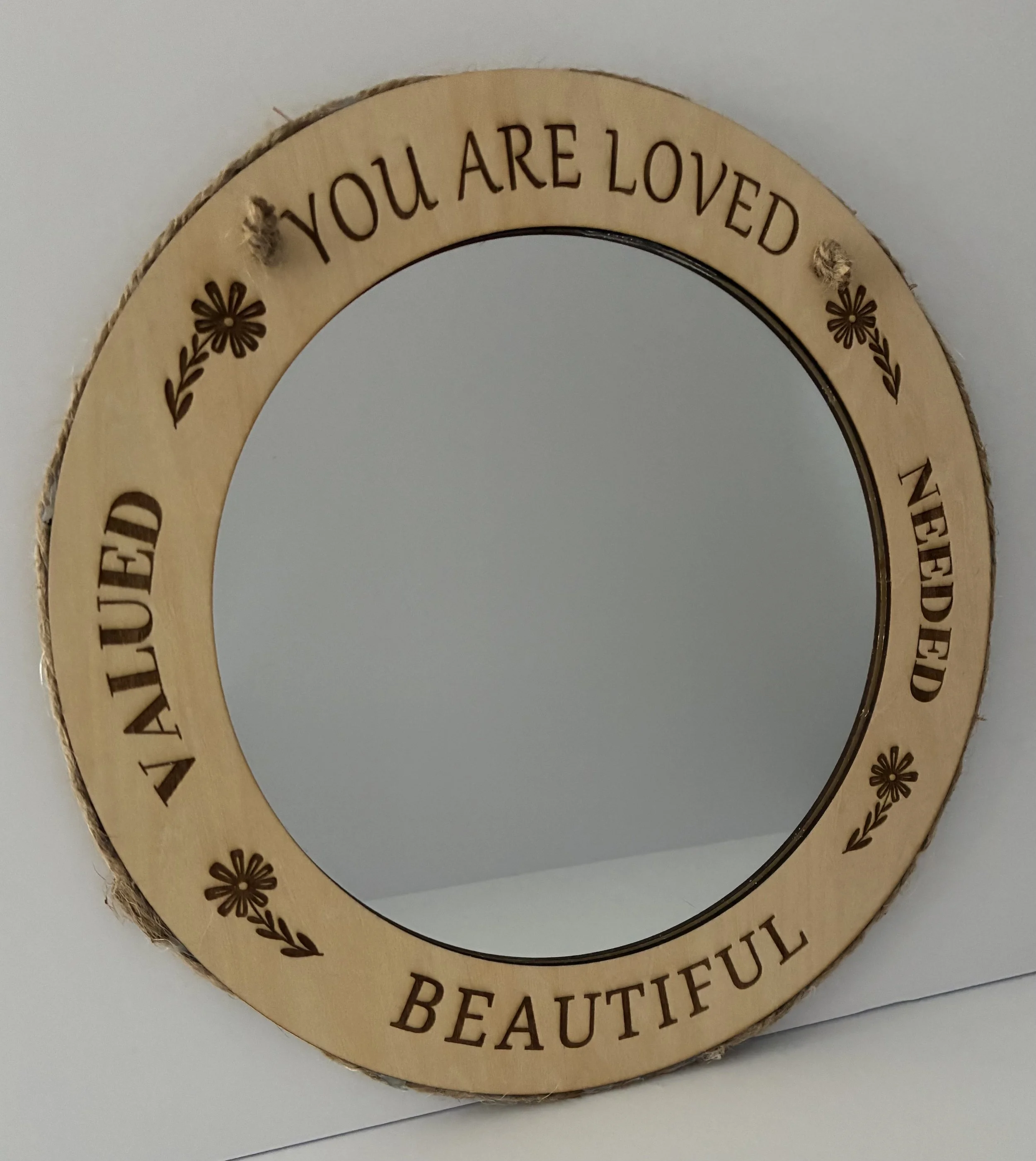 Round mirror with a wooden frame engraved with the words 'You are loved,' 'Sweet,' 'Nefed,' and 'Beautiful,' decorated with small flower designs.