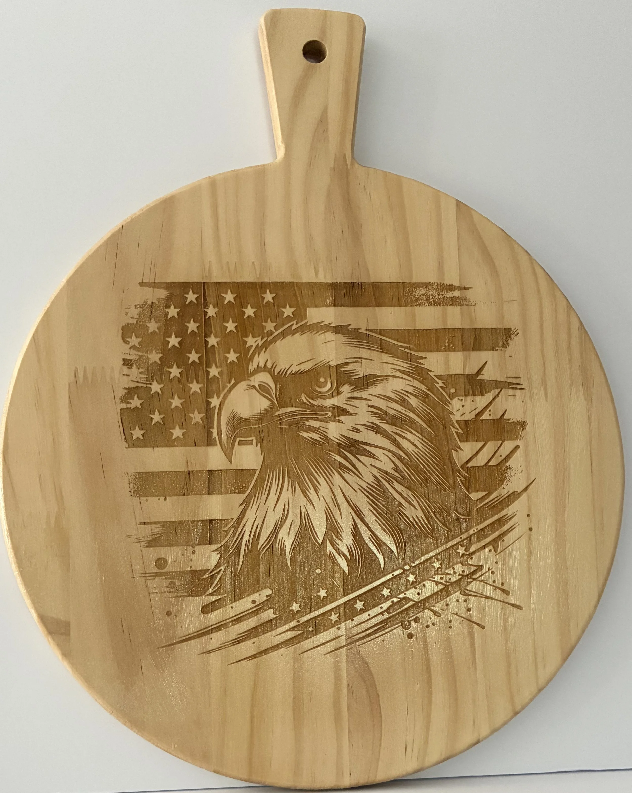 Round wooden cutting board with a handle, featuring a printed American flag and a detailed illustration of an eagle's head.