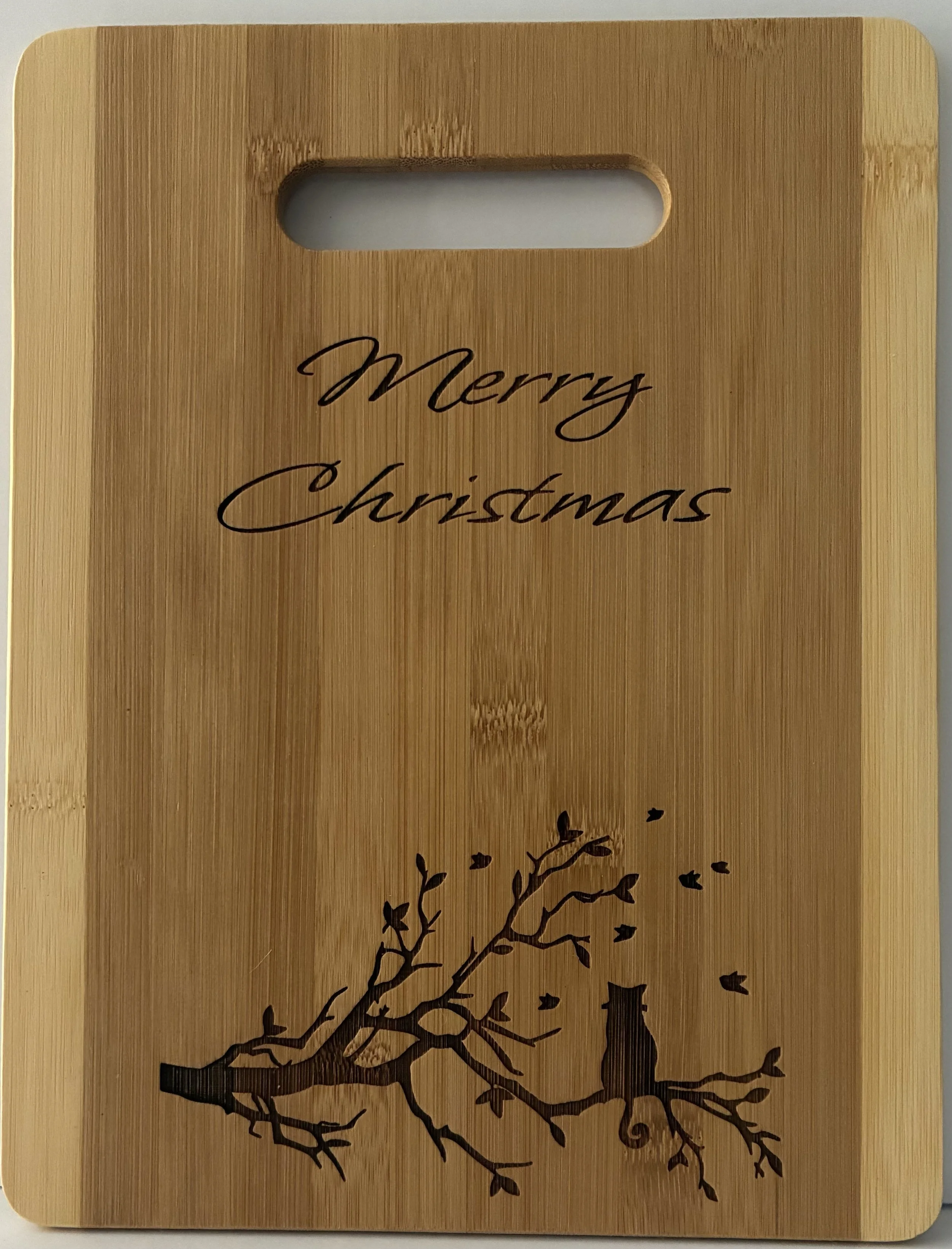 Wooden cutting board with 'Merry Christmas' text and a silhouette of a cat sitting on a tree branch with falling leaves.
