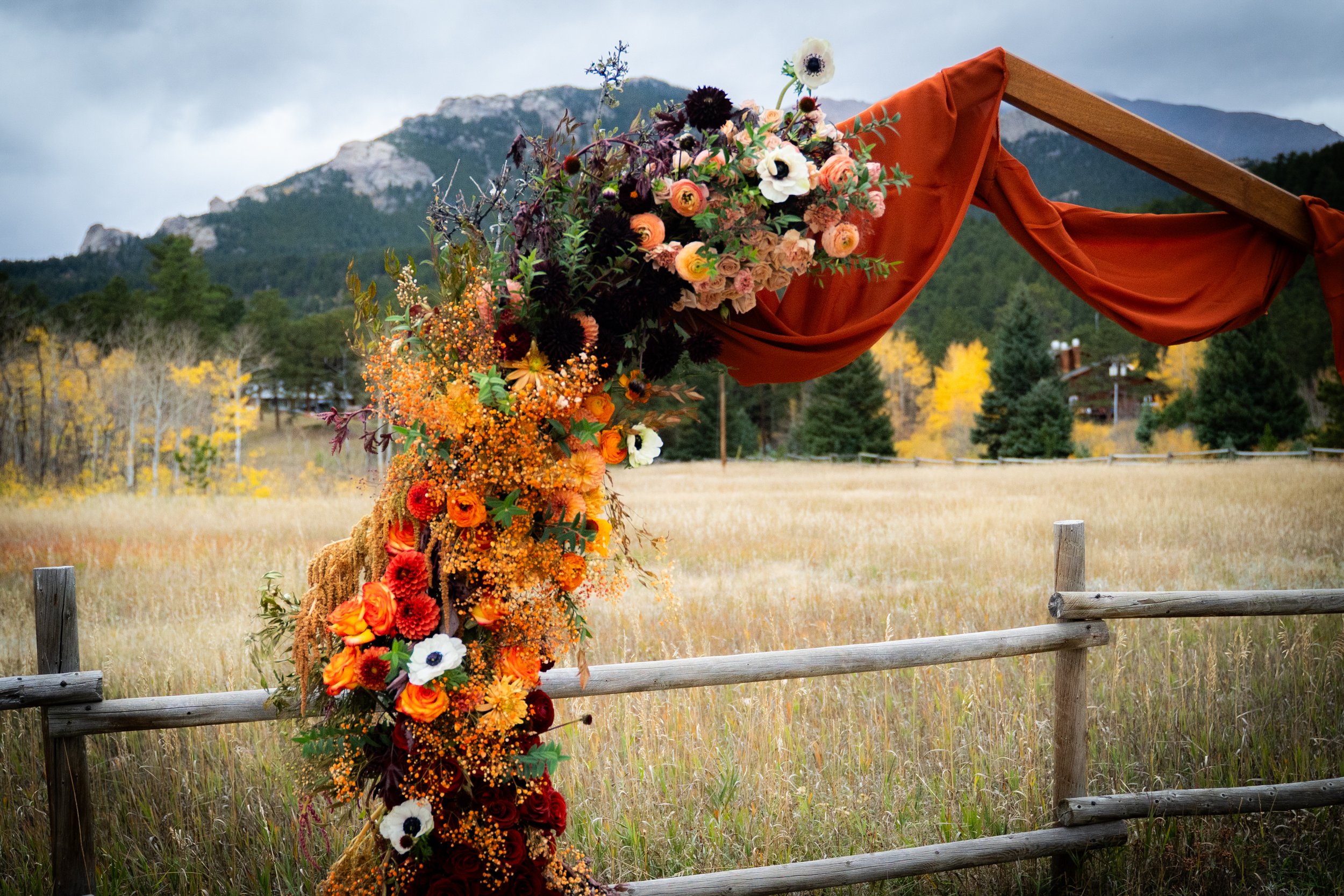 Colorado mountain wedding floral install by Ash + Ether, featuring warm autumn colors and draped fabric.