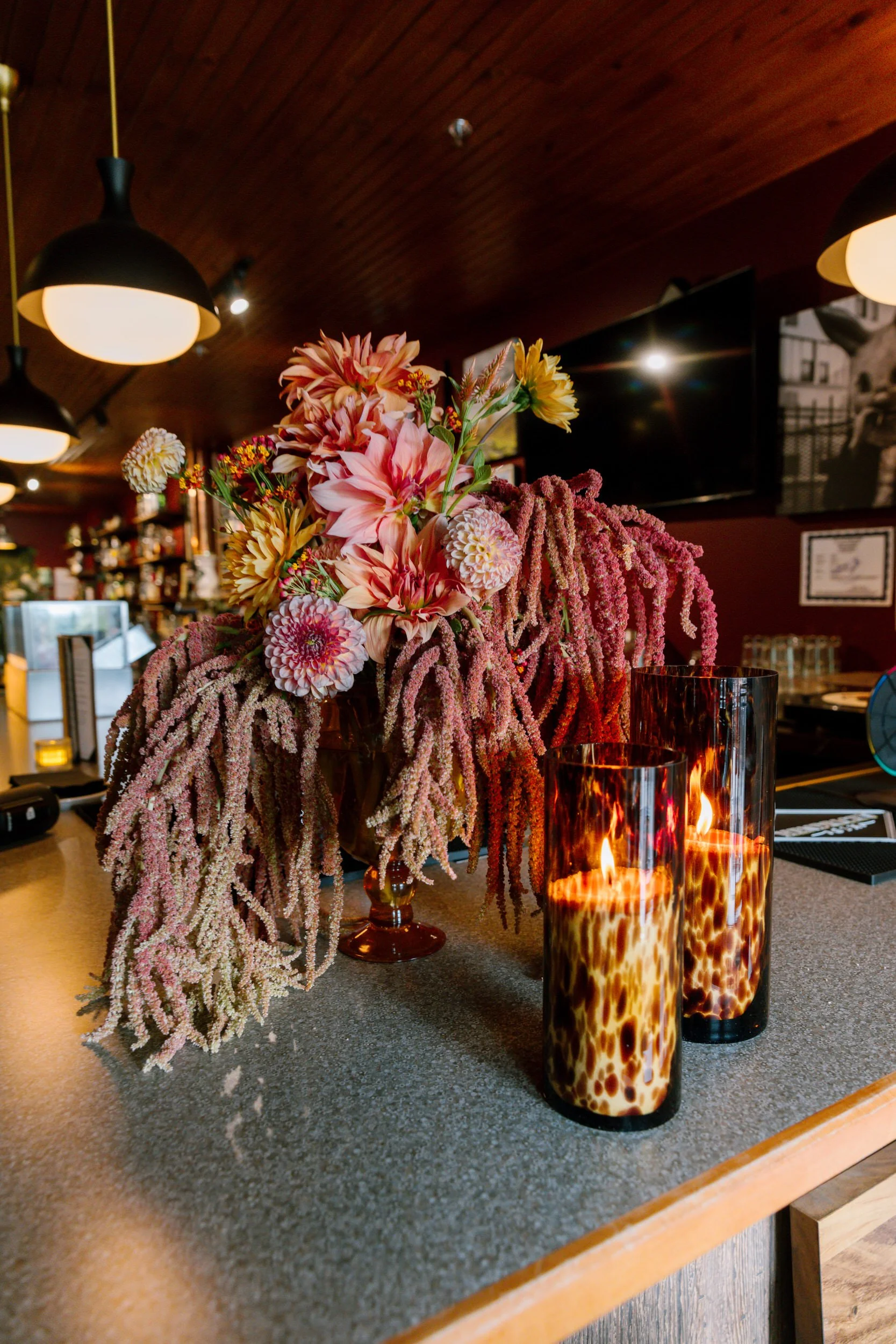 A larger floral arrangement on a table with two tall candles in front of it