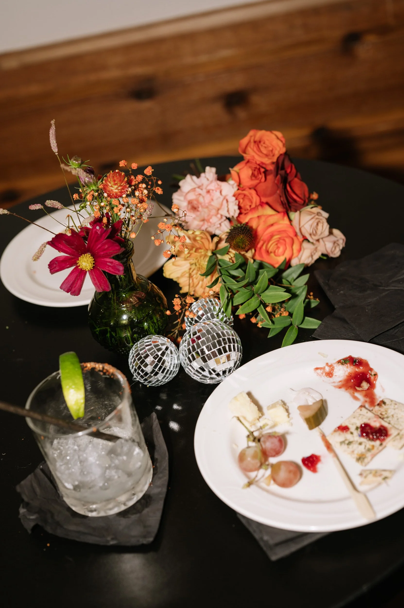 A reception table with a plate of half eaten food, a drink, small floral arrangements, and mini disco balls