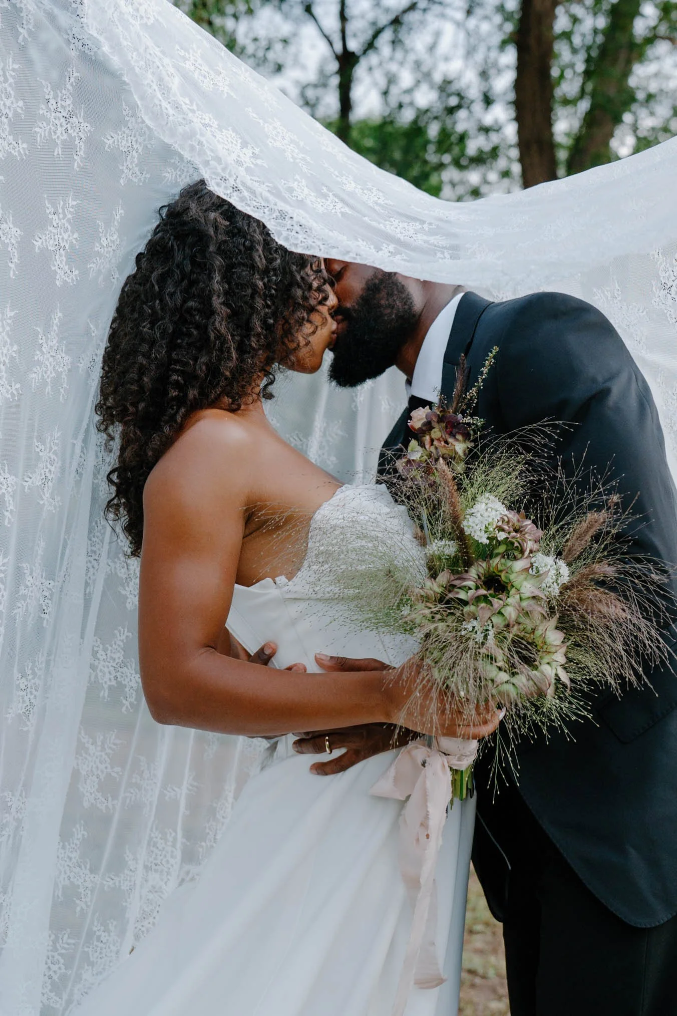 A newlywed couple kissing while one is holding a bouquet of flowers