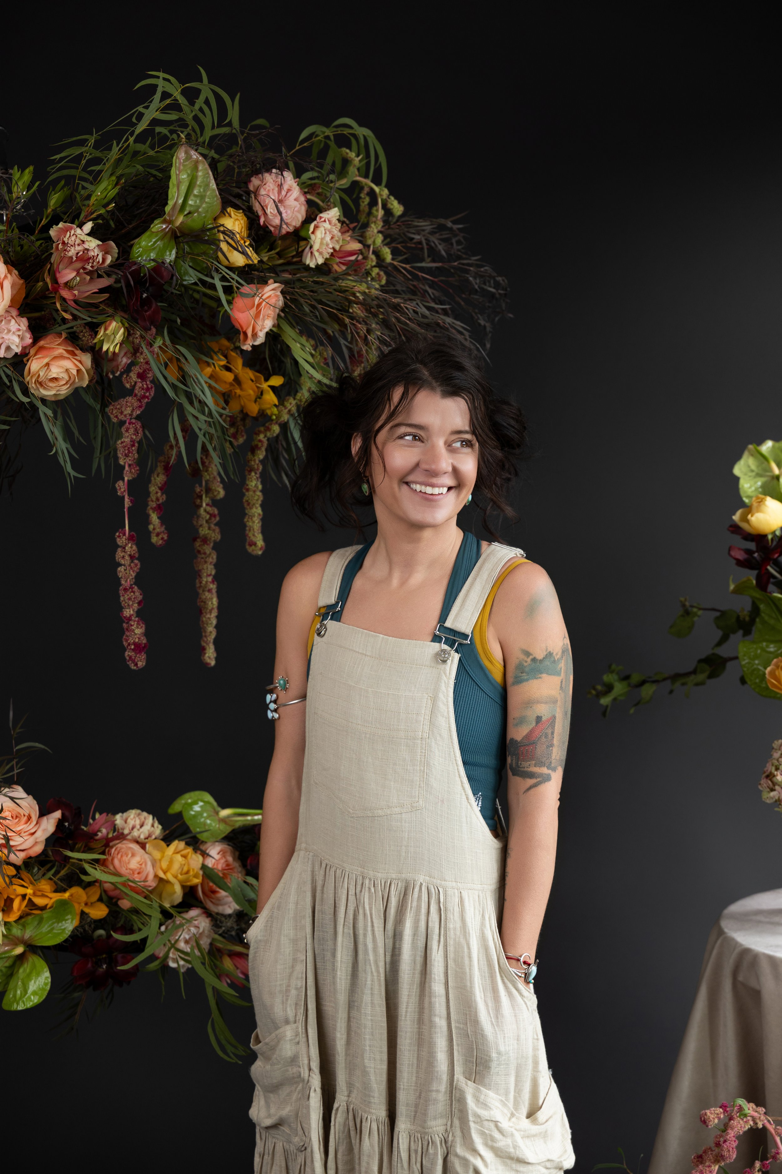 Ash smiling with her hands in her pockets and florals all around her