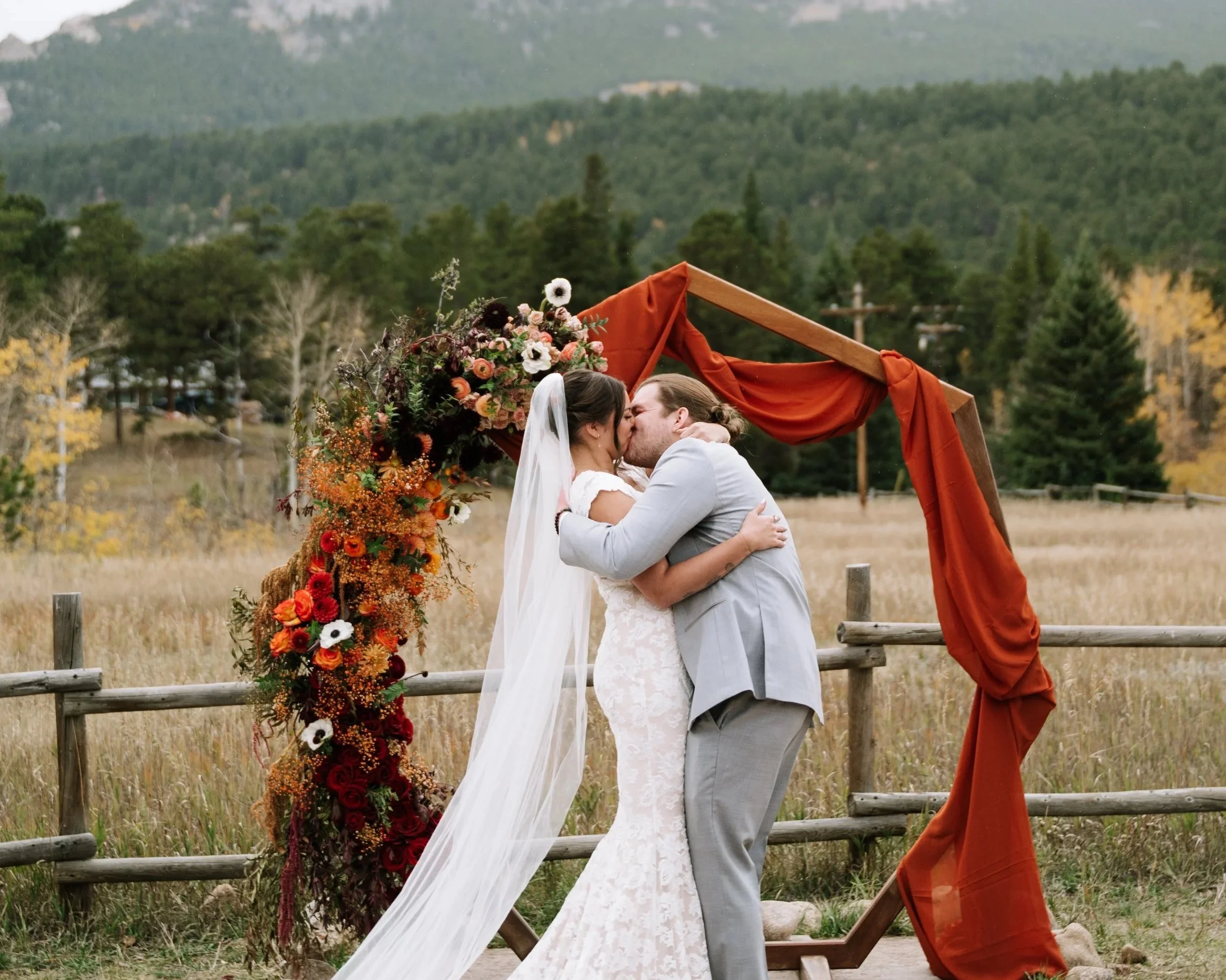 Bride and groom kissing beneath an Ash + Ether floral arch at a Colorado mountain wedding.