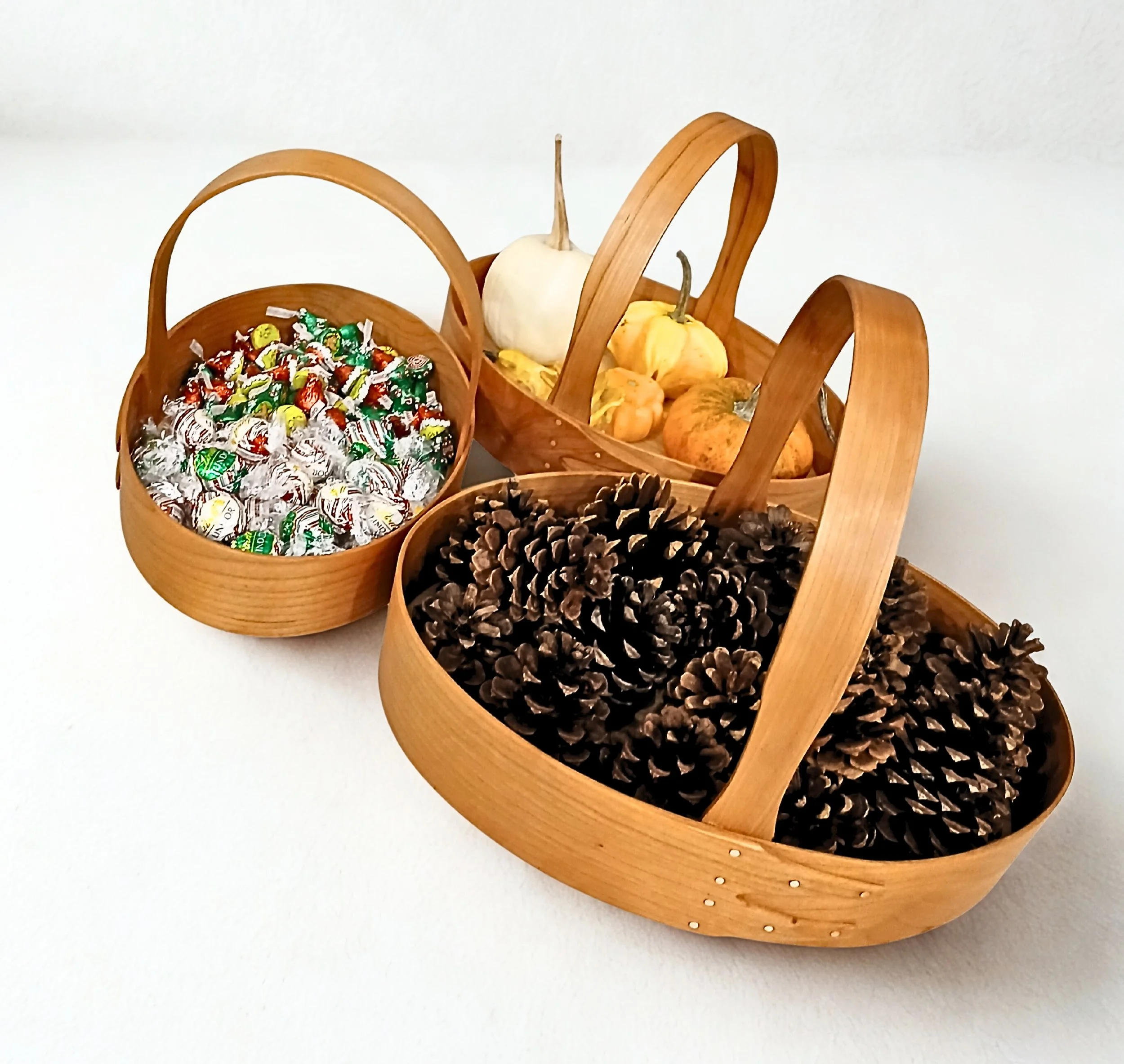 Three wooden baskets filled with small candies, mini pumpkins, and pinecones on a white background.