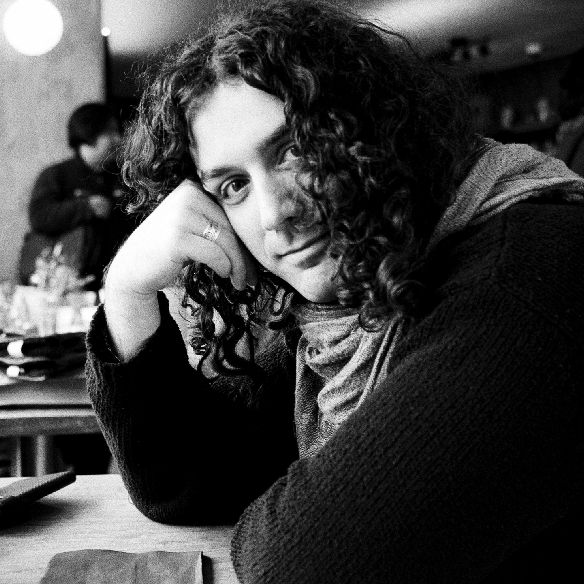 A man with curly hair resting her head on her hand, looking at the camera in a casual setting.