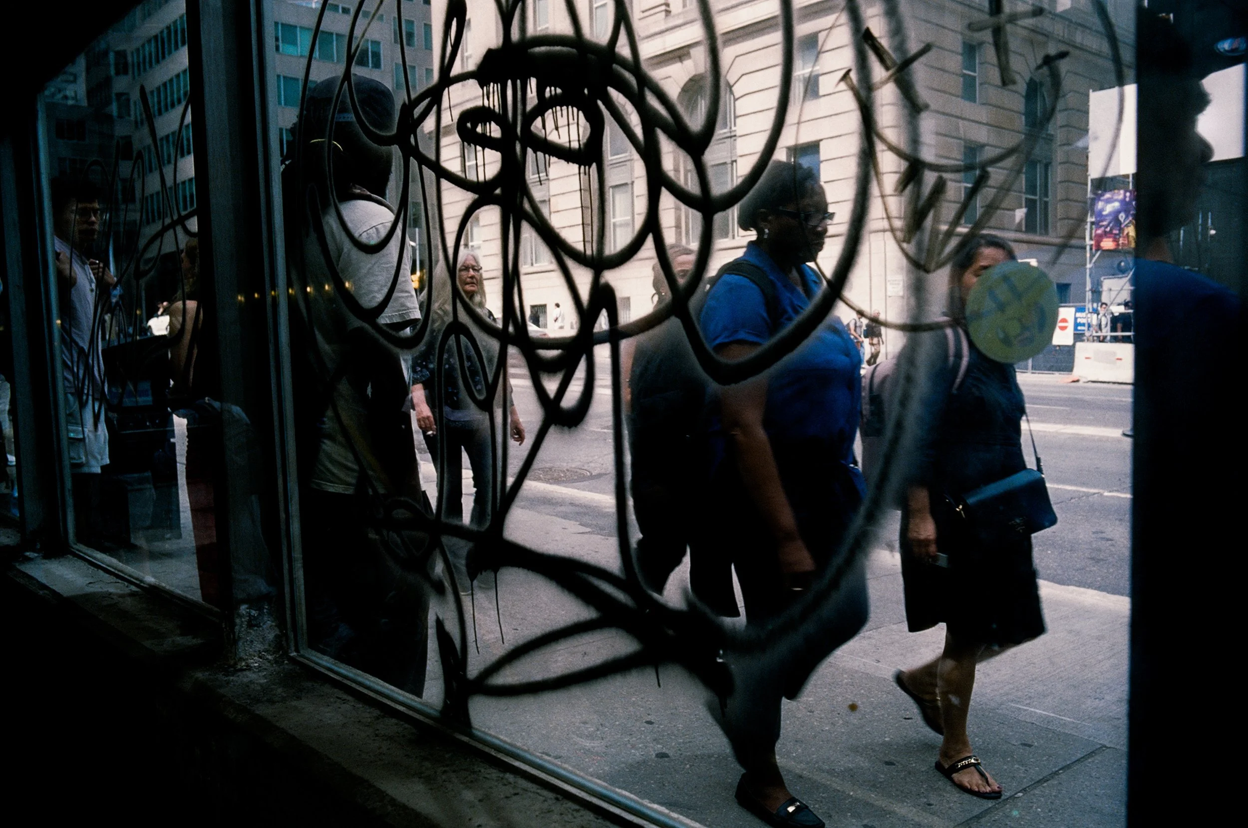 People walking outside viewed through a store window with black decorative metalwork.