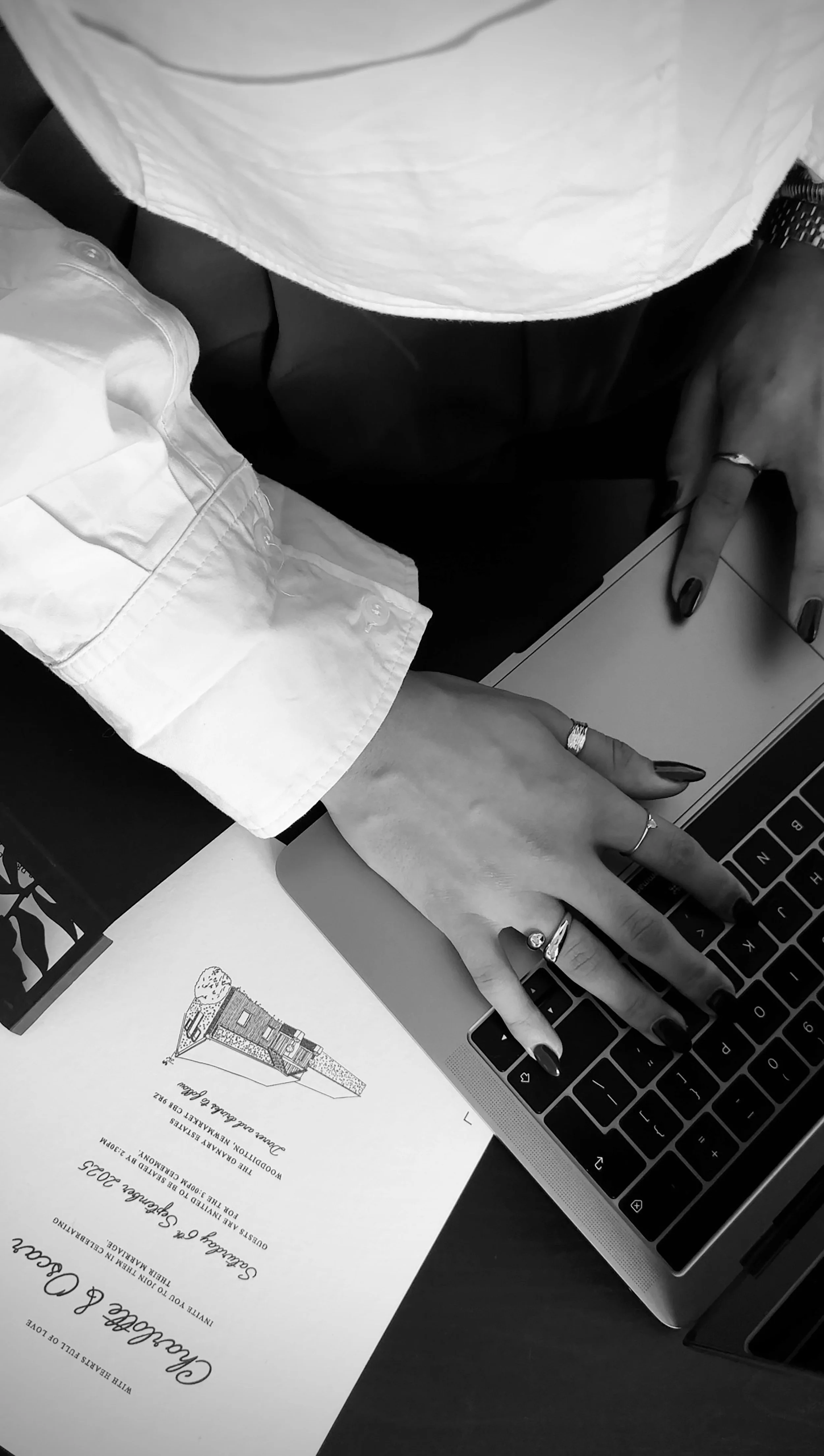 A person using a laptop at a desk, with a wedding invitation or program on the desk.