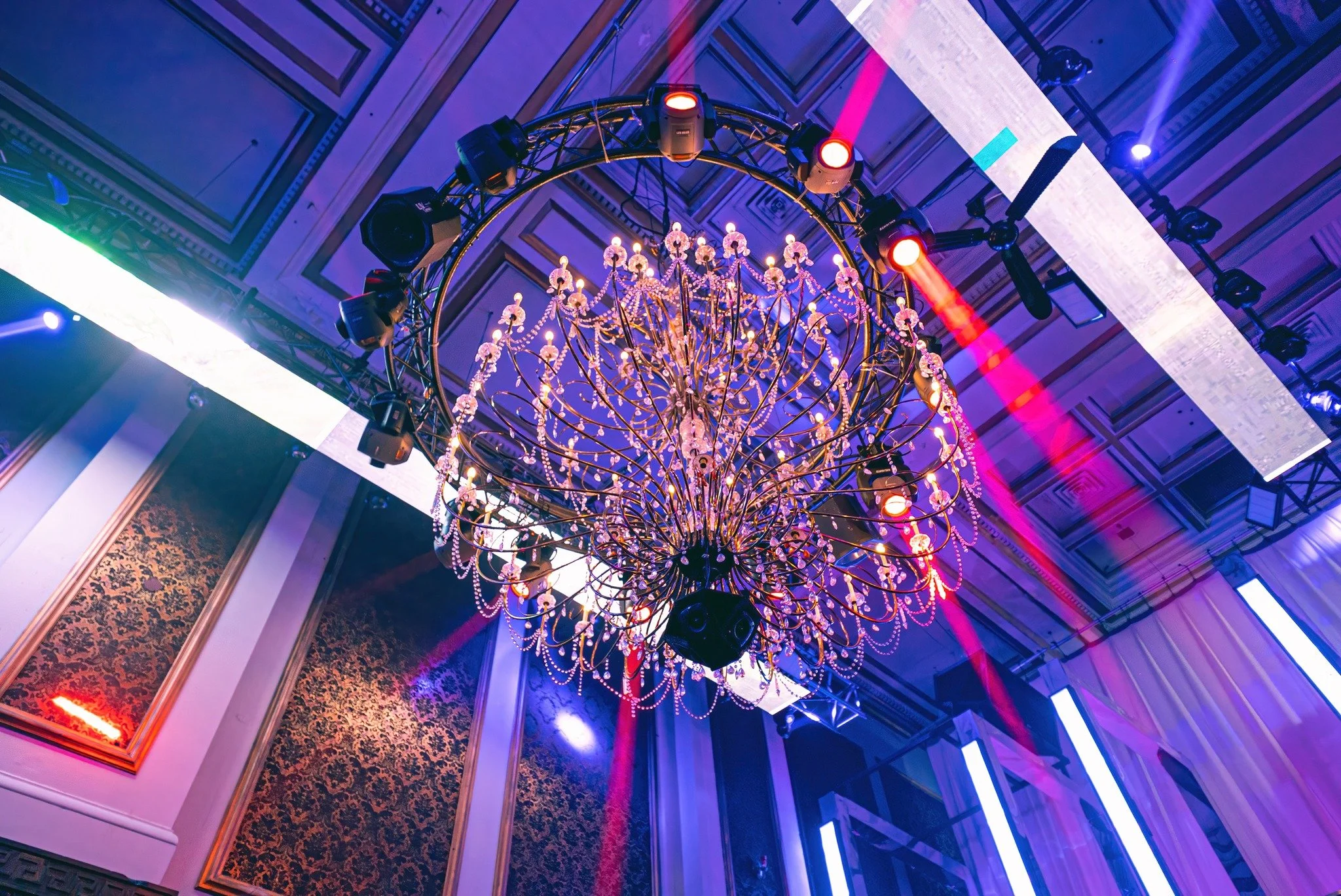 Elegant ballroom with large ornate chandelier, colorful lighting effects, and decorative walls.