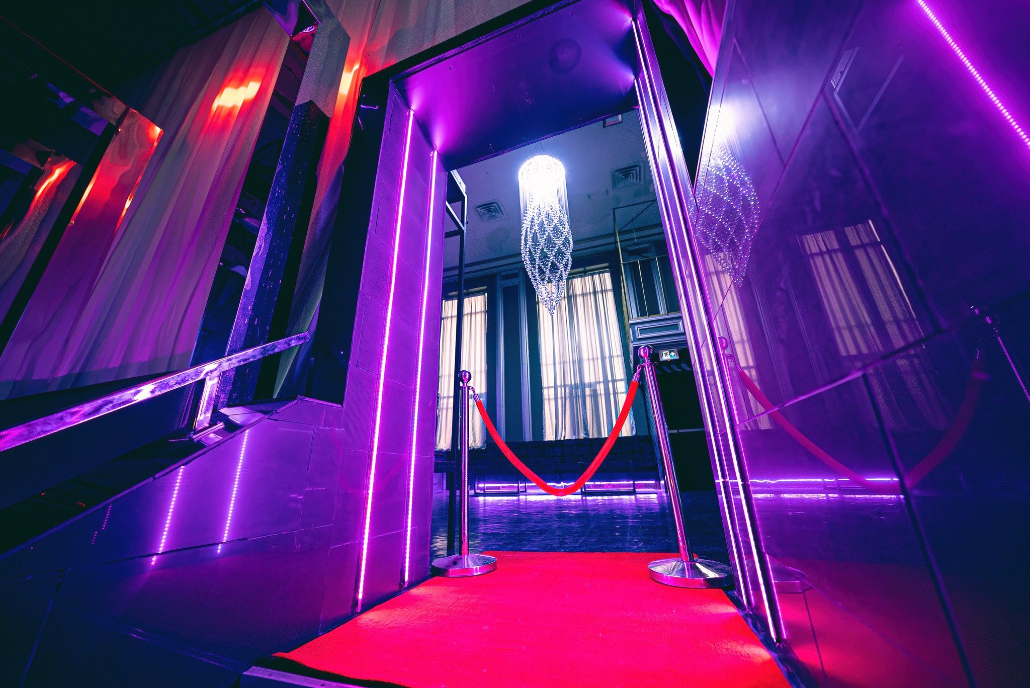 Elegant entrance with a red carpet, purple neon lights, and a chandelier hanging from the ceiling.