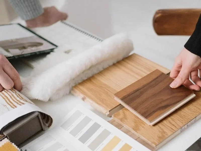People selecting wood and laminate flooring samples on a table with color swatches and sample booklets.