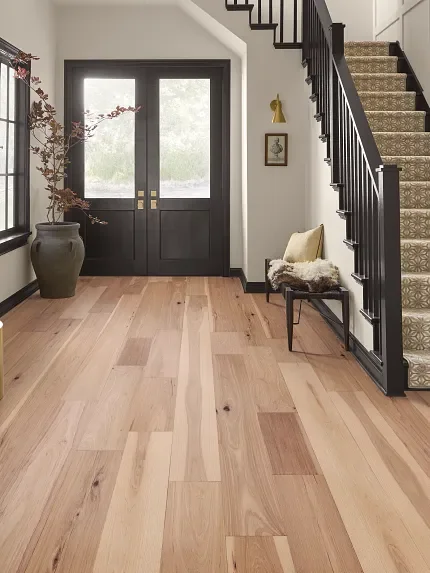 Entryway with wooden flooring, black front door with glass panels, potted plant, small bench with cushion, and staircase with patterned carpet and black railing.