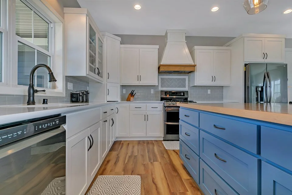 Modern kitchen with white cabinets, a blue island, stainless steel appliances, wooden countertops, and hardwood flooring.