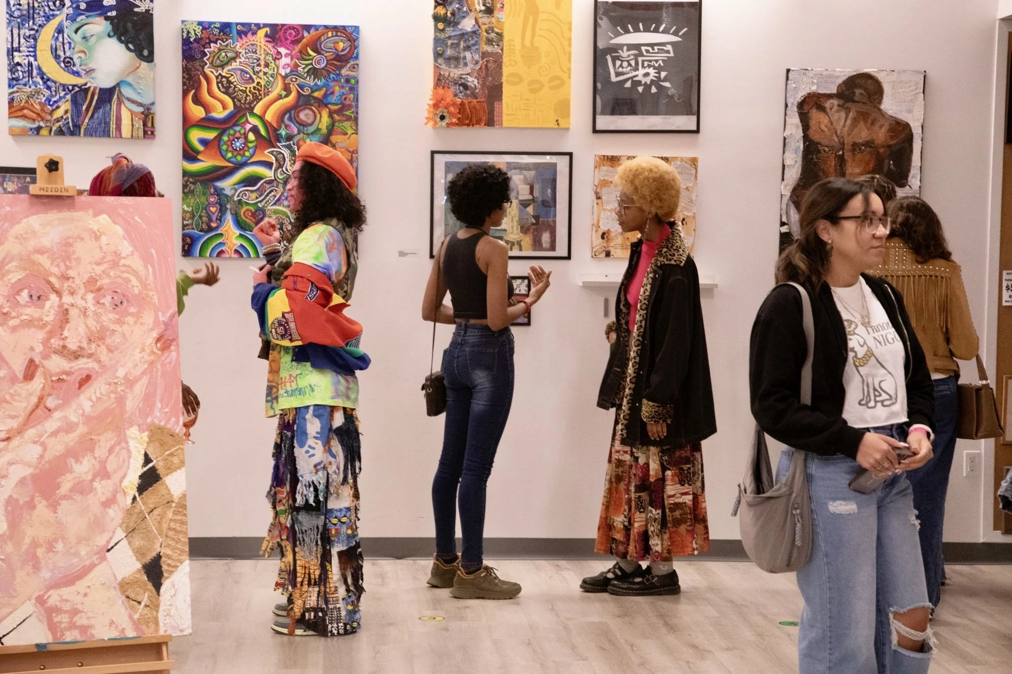 People in an art gallery viewing various colorful paintings on the wall.