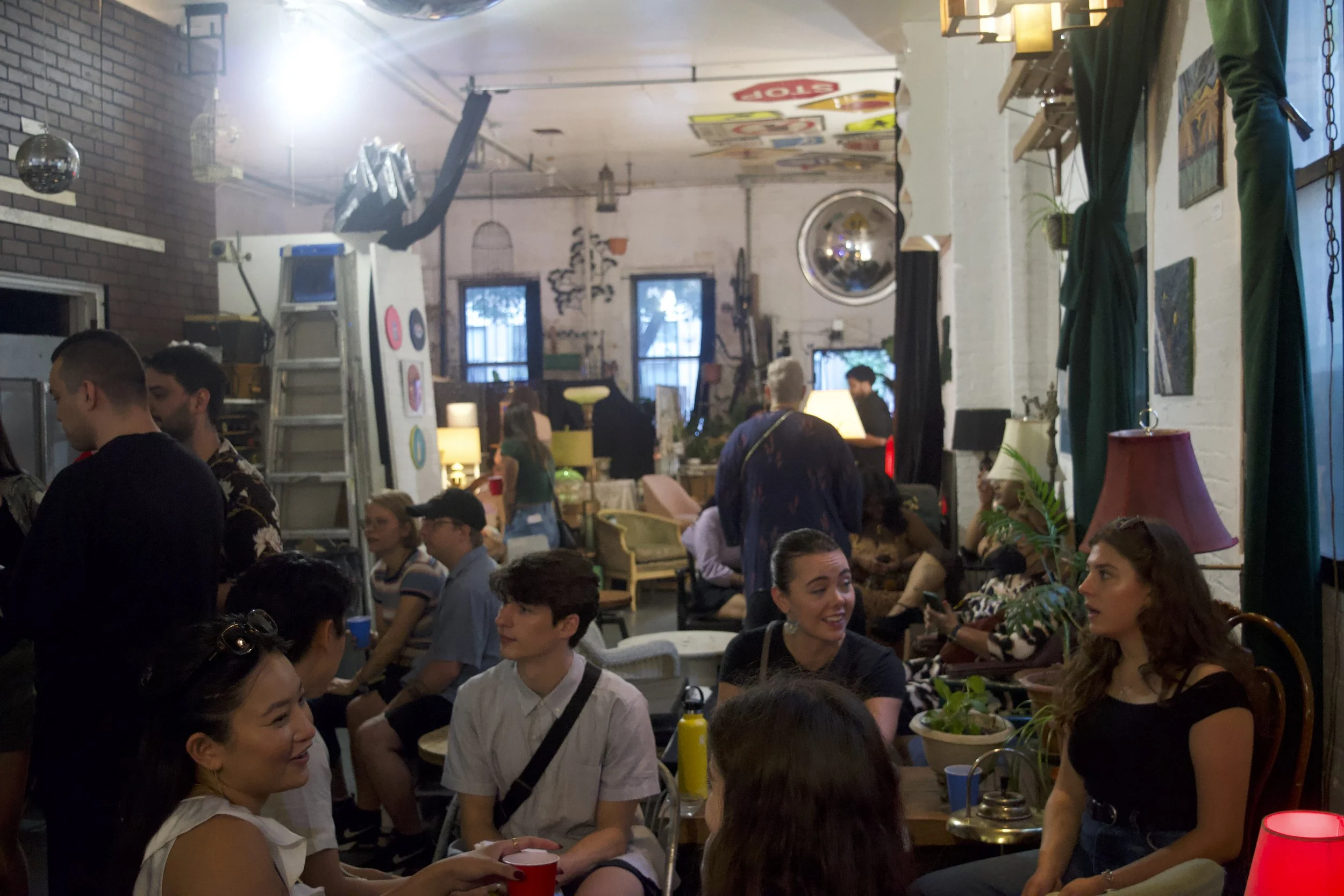Indoor gathering of people socializing in a cozy, eclectic space with vintage decor and warm lighting.