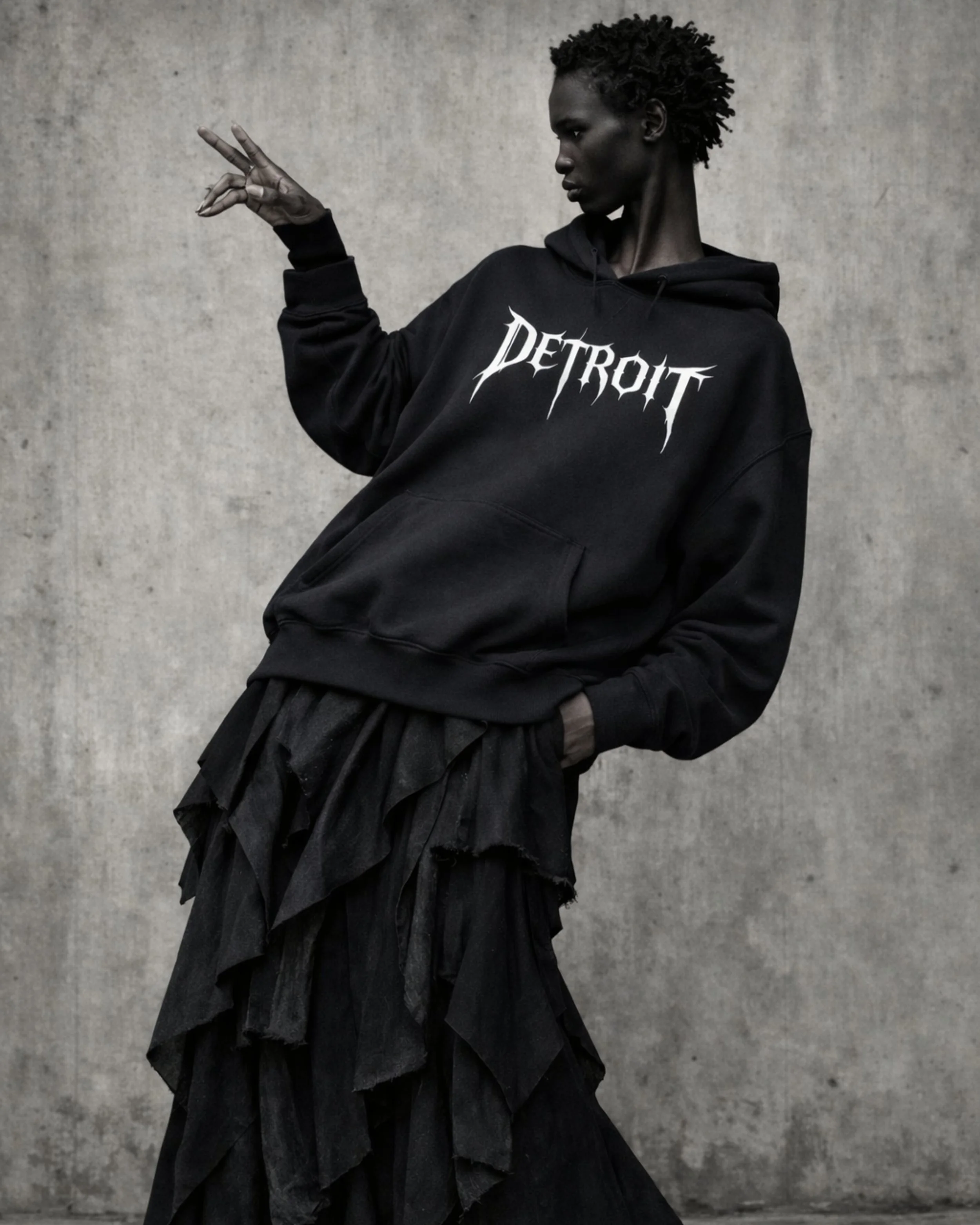 Avant-garde oversized black hoodie by Techno Studios featuring the Detroit graphic. Shot in a brutalist concrete environment, this underground techno culture garment blends industrial aesthetics with contemporary experimental fashion.